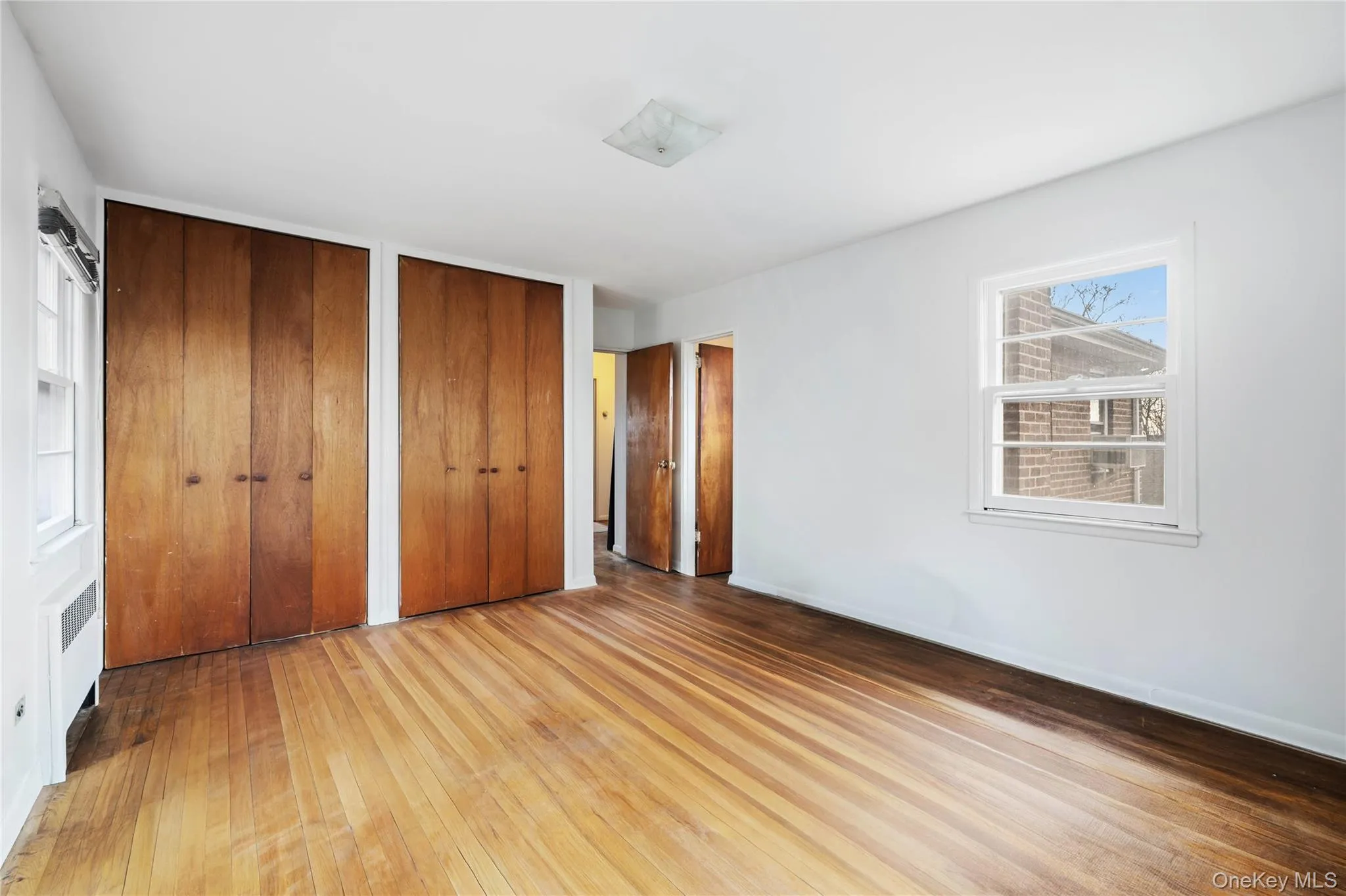Unfurnished bedroom featuring wood-type flooring, multiple closets, and radiator heating unit Unfurnished bedroom featuring wood-type flooring, multiple closets, and radiator heating unit