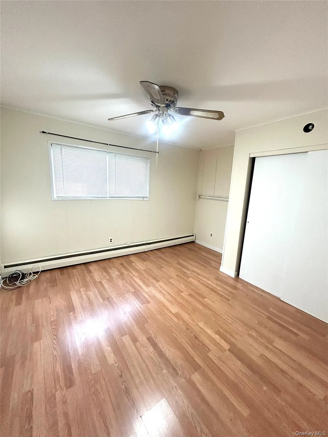 Unfurnished bedroom featuring light wood finished floors, a ceiling fan, baseboard heating, and a closet Unfurnished bedroom featuring light wood finished floors, a ceiling fan, baseboard heating, and a closet