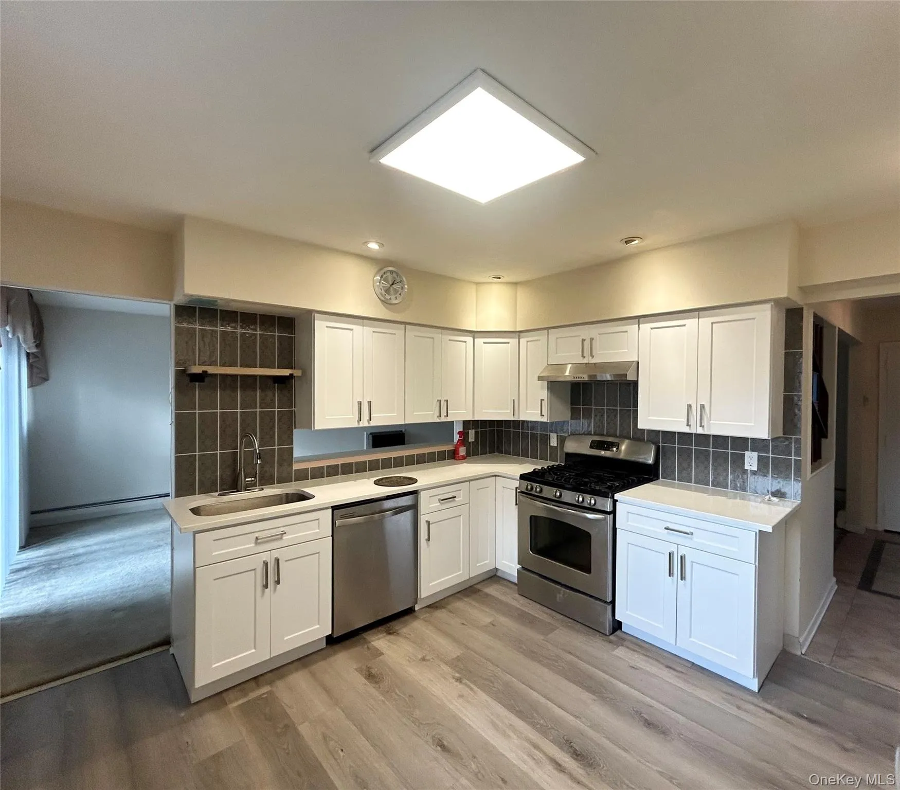 Kitchen featuring appliances with stainless steel finishes, white cabinetry, backsplash, light wood-style floors, and under cabinet range hood Kitchen featuring appliances with stainless steel finishes, white cabinetry, backsplash, light wood-style floors, and under cabinet range hood