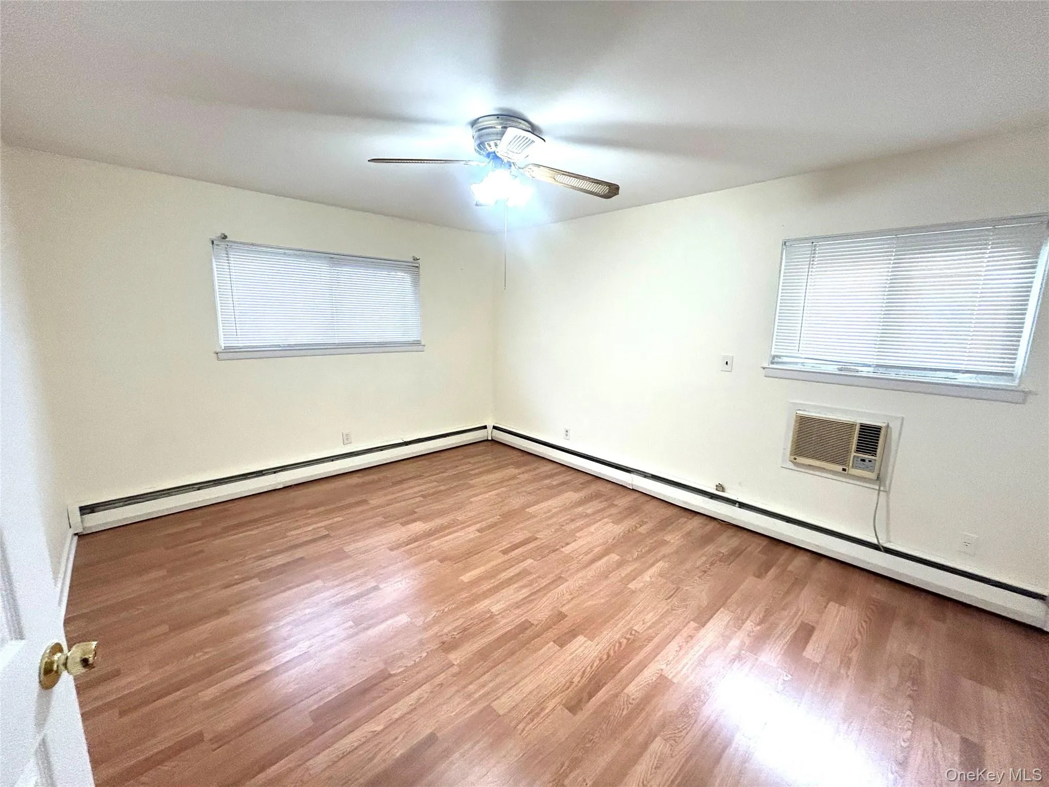 Spare room featuring baseboard heating, light wood finished floors, and a wall mounted AC Spare room featuring baseboard heating, light wood finished floors, and a wall mounted AC