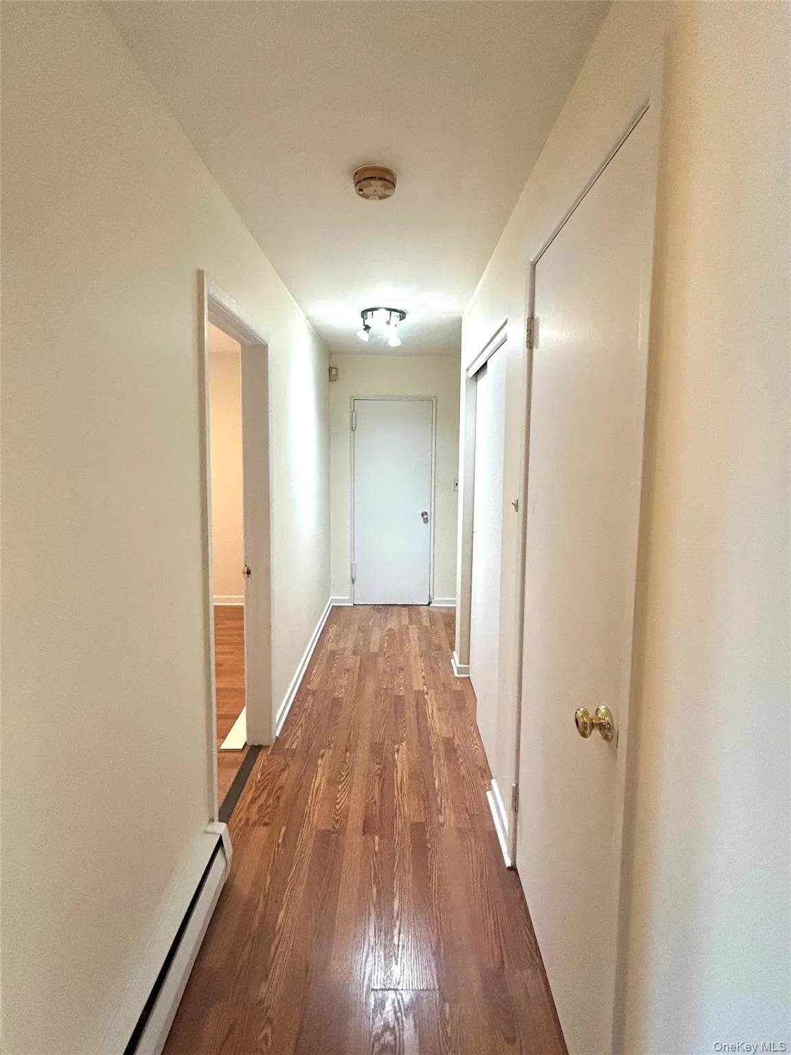 Hall featuring a baseboard heating unit and wood finished floors Hall featuring a baseboard heating unit and wood finished floors