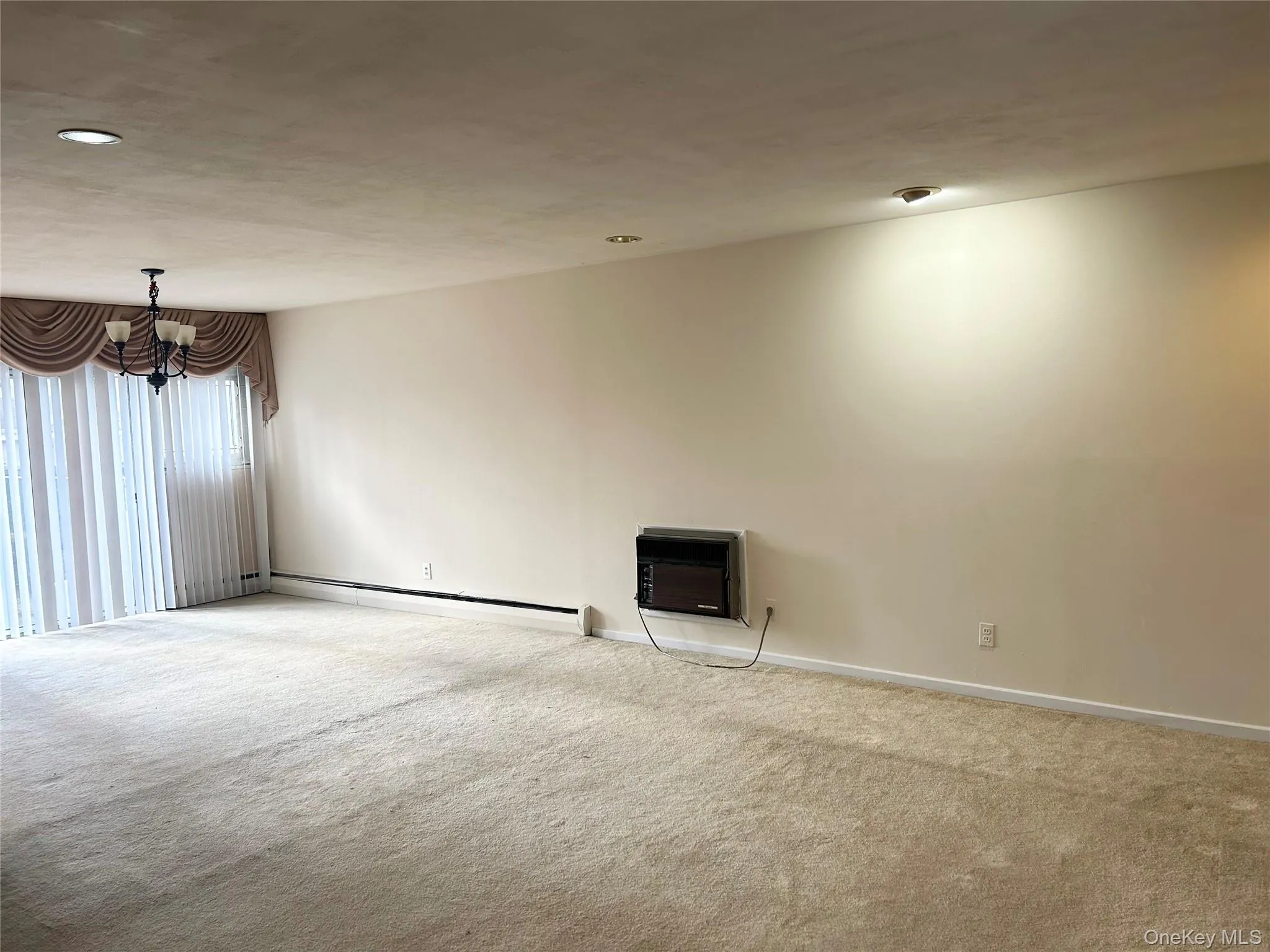Carpeted empty room featuring baseboard heating, a chandelier, and heating unit Carpeted empty room featuring baseboard heating, a chandelier, and heating unit