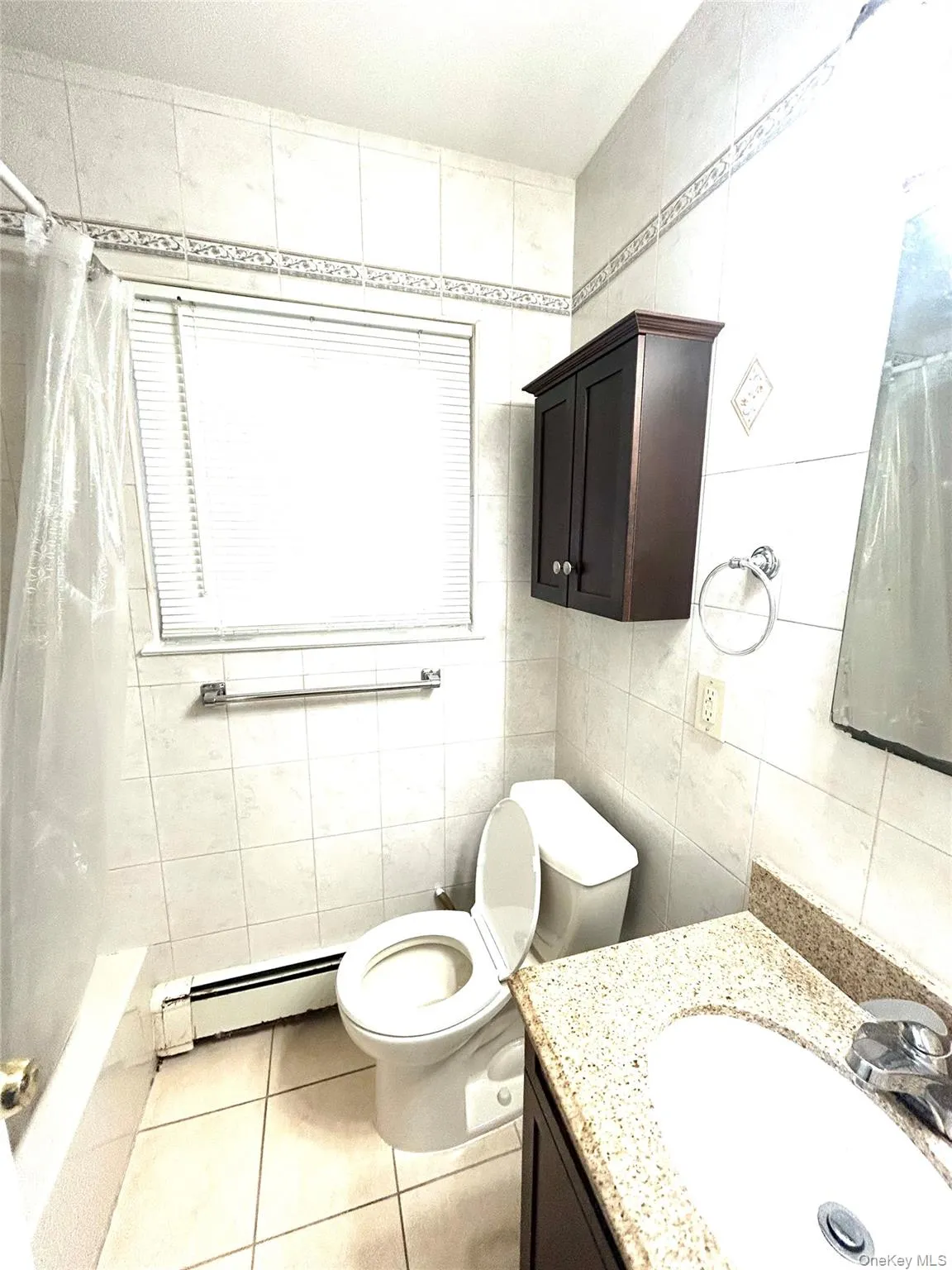 Bathroom with light tile patterned floors, a baseboard radiator, vanity, tile walls, and shower / tub combo with curtain Bathroom with light tile patterned floors, a baseboard radiator, vanity, tile walls, and shower / tub combo with curtain