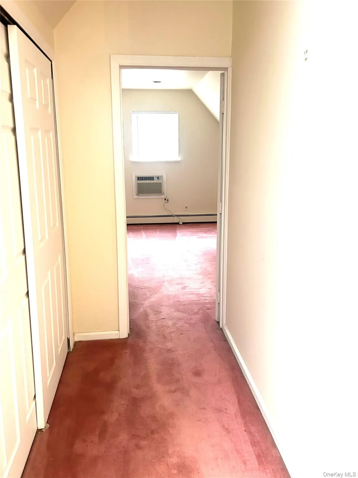 Corridor featuring lofted ceiling, carpet floors, an AC wall unit, and a baseboard radiator Corridor featuring lofted ceiling, carpet floors, an AC wall unit, and a baseboard radiator