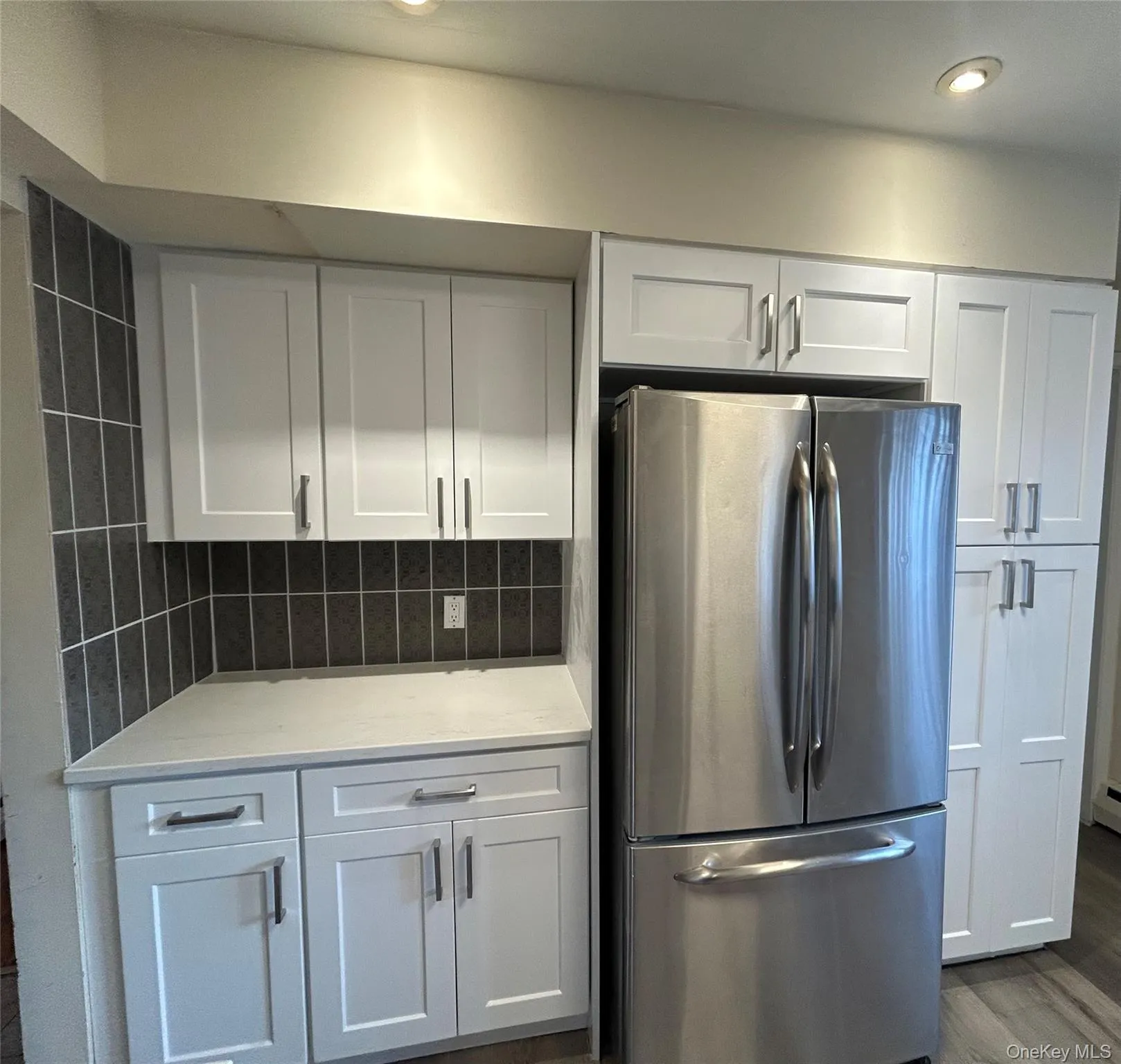 Kitchen featuring freestanding refrigerator, white cabinets, light stone counters, dark wood-style floors, and tasteful backsplash Kitchen featuring freestanding refrigerator, white cabinets, light stone counters, dark wood-style floors, and tasteful backsplash