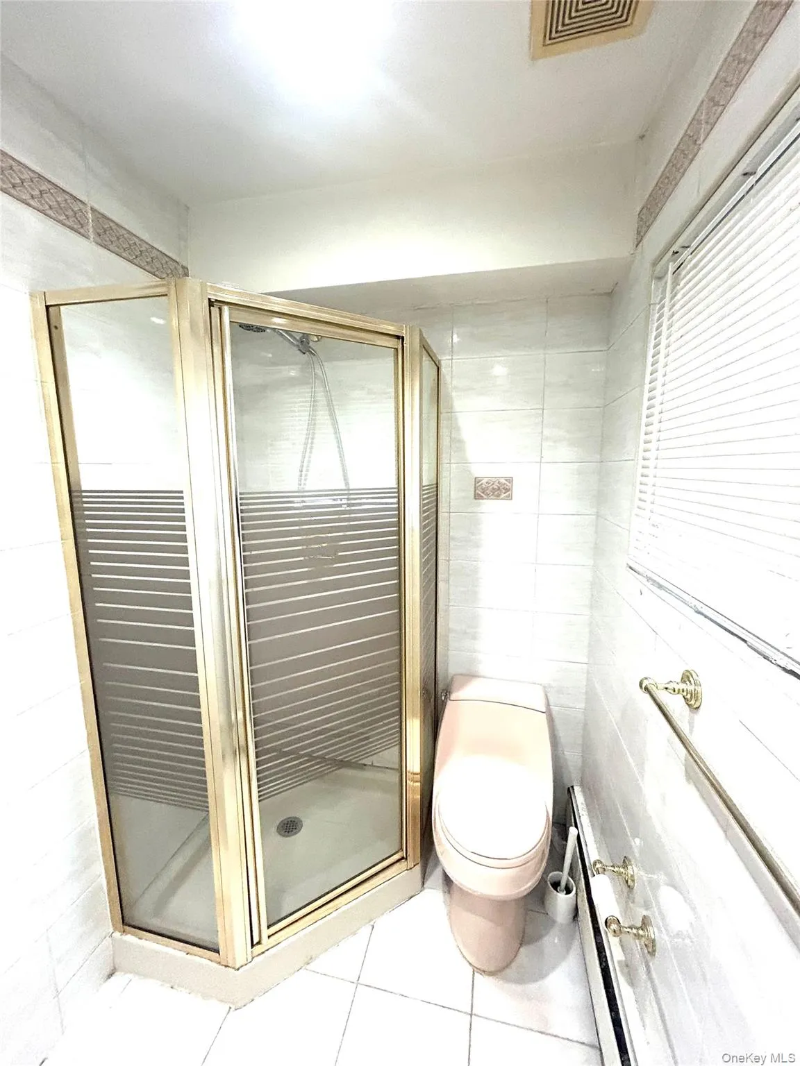 Bathroom featuring a stall shower, tile walls, light tile patterned floors, and baseboard heating Bathroom featuring a stall shower, tile walls, light tile patterned floors, and baseboard heating