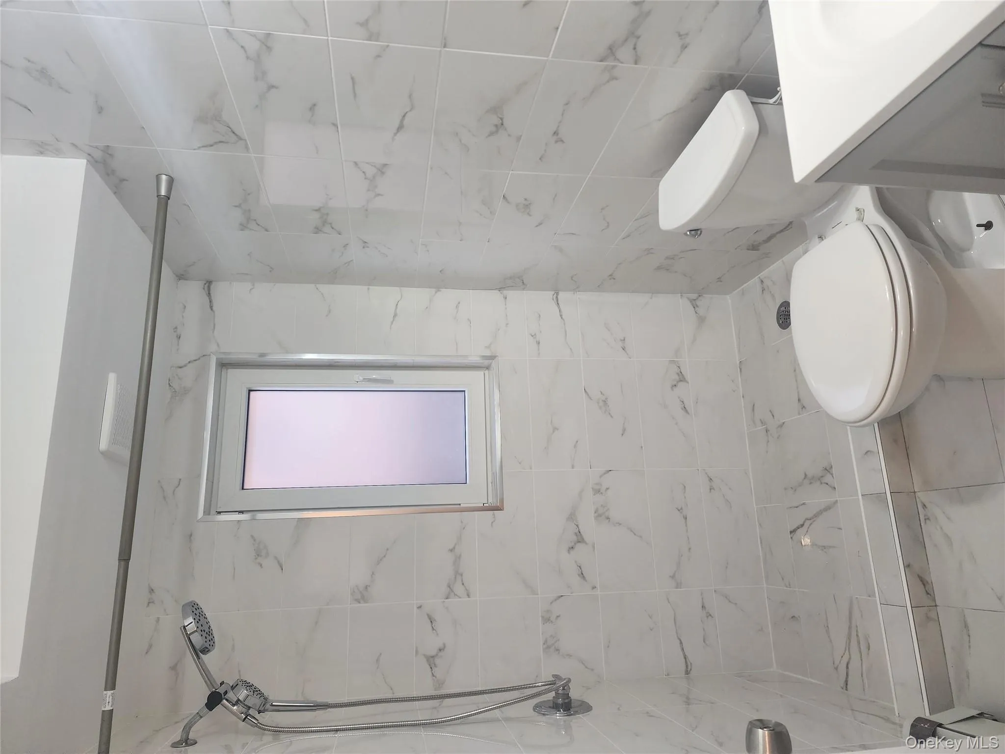 Bathroom featuring a marble finish shower, vanity, marble look tiles, and tile walls Bathroom featuring a marble finish shower, vanity, marble look tiles, and tile walls