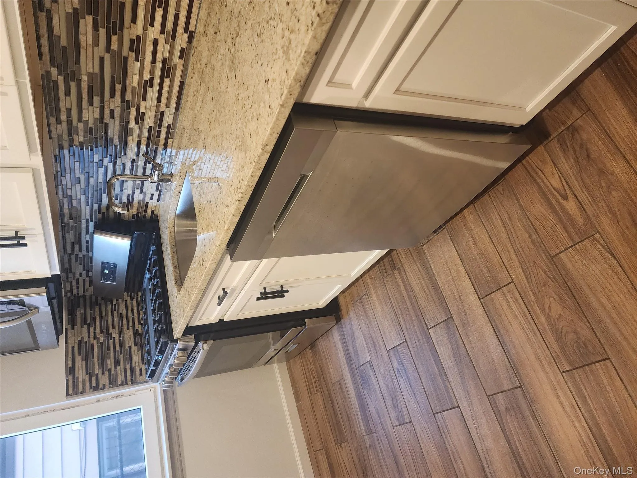 Kitchen featuring stainless steel appliances, white cabinetry, dark wood finished floors, and light stone counters Kitchen featuring stainless steel appliances, white cabinetry, dark wood finished floors, and light stone counters