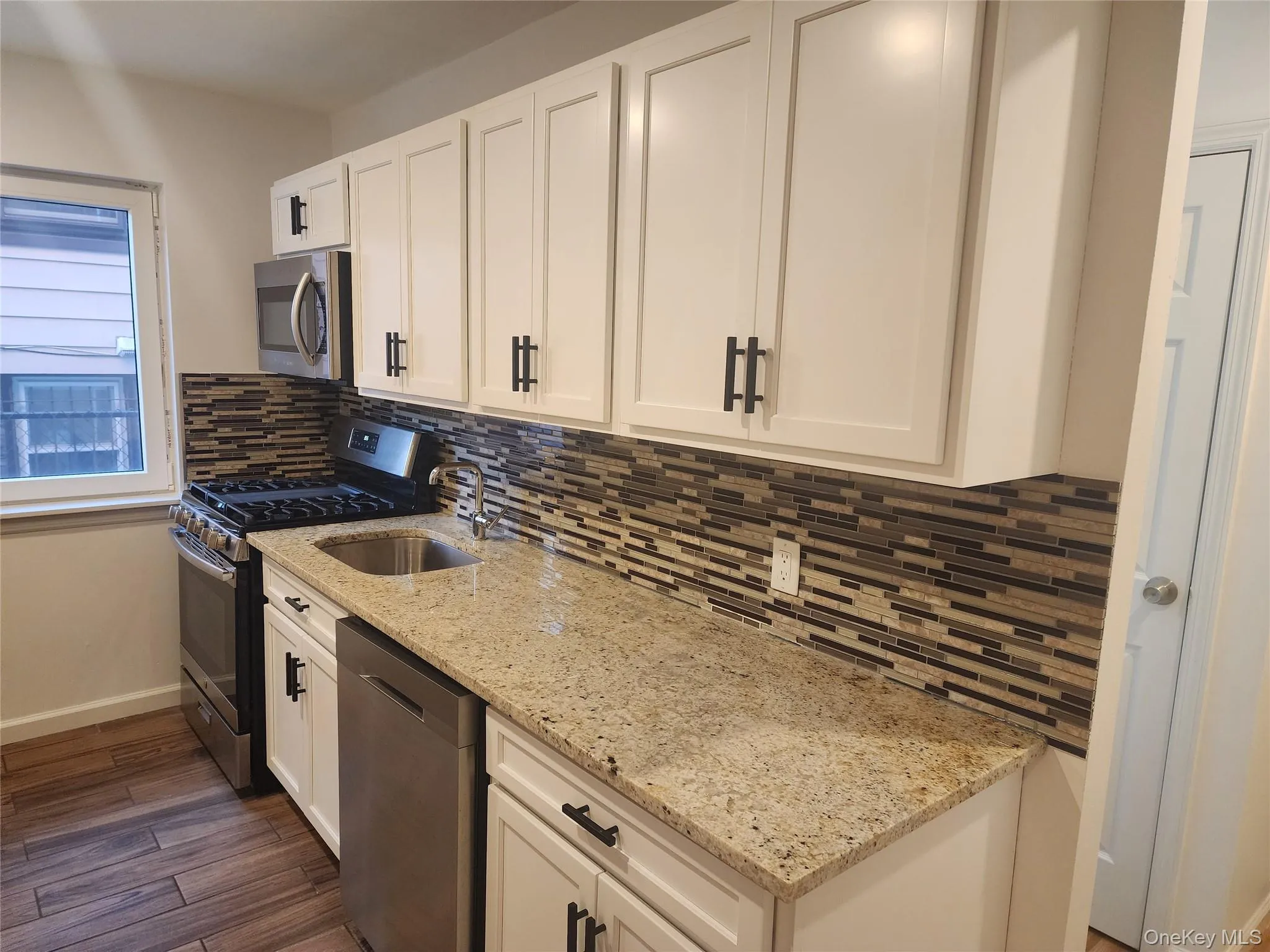 Kitchen featuring appliances with stainless steel finishes, white cabinetry, light stone countertops, and dark wood finished floors Kitchen featuring appliances with stainless steel finishes, white cabinetry, light stone countertops, and dark wood finished floors
