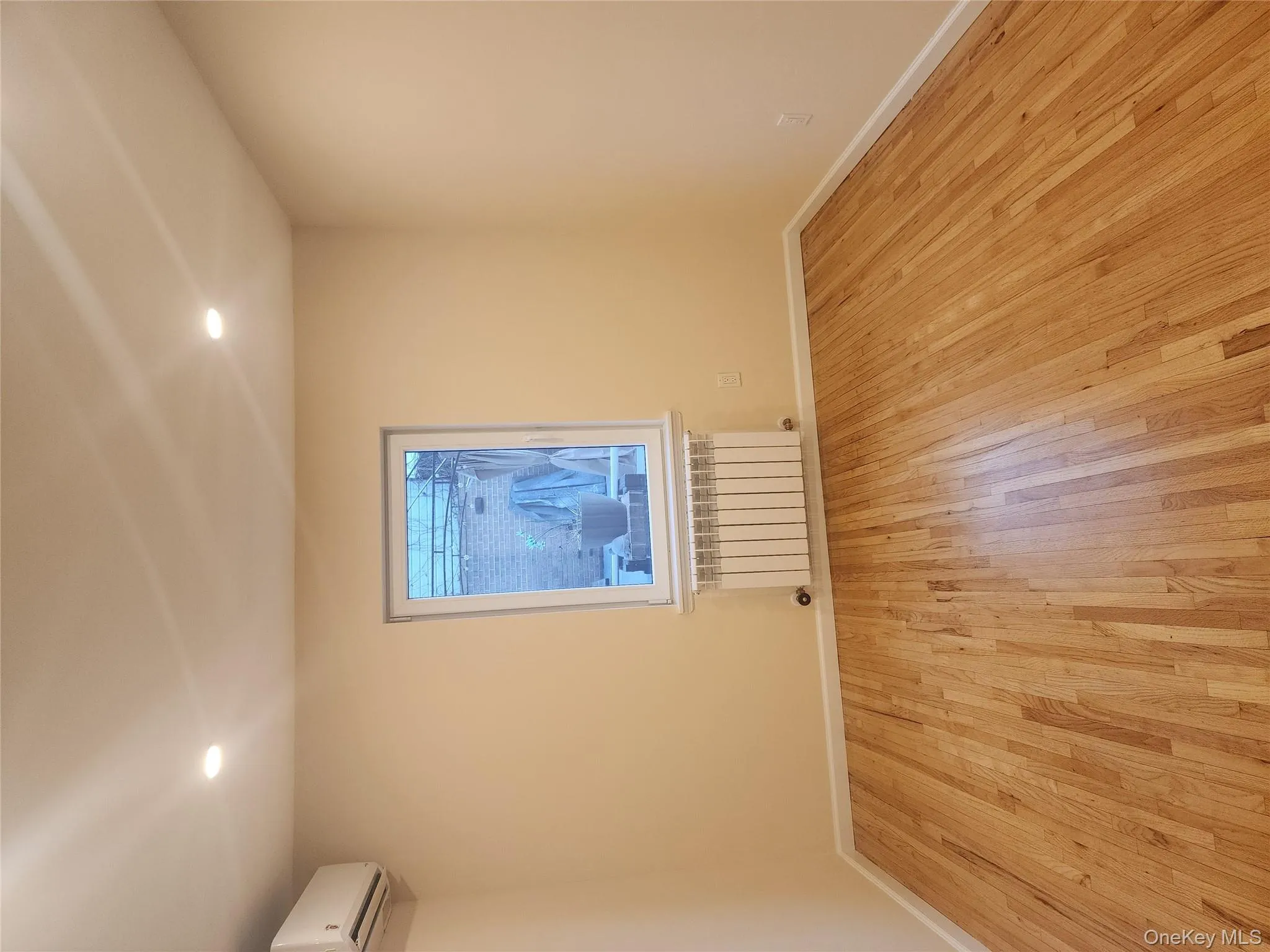 Spare room with radiator heating unit, recessed lighting, light wood-type flooring, and a wall mounted air conditioner Spare room with radiator heating unit, recessed lighting, light wood-type flooring, and a wall mounted air conditioner