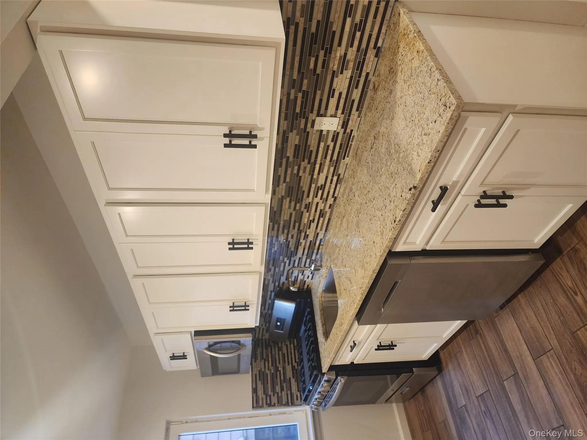 Kitchen featuring white cabinets, stainless steel appliances, light stone counters, dark wood finished floors, and decorative backsplash Kitchen featuring white cabinets, stainless steel appliances, light stone counters, dark wood finished floors, and decorative backsplash