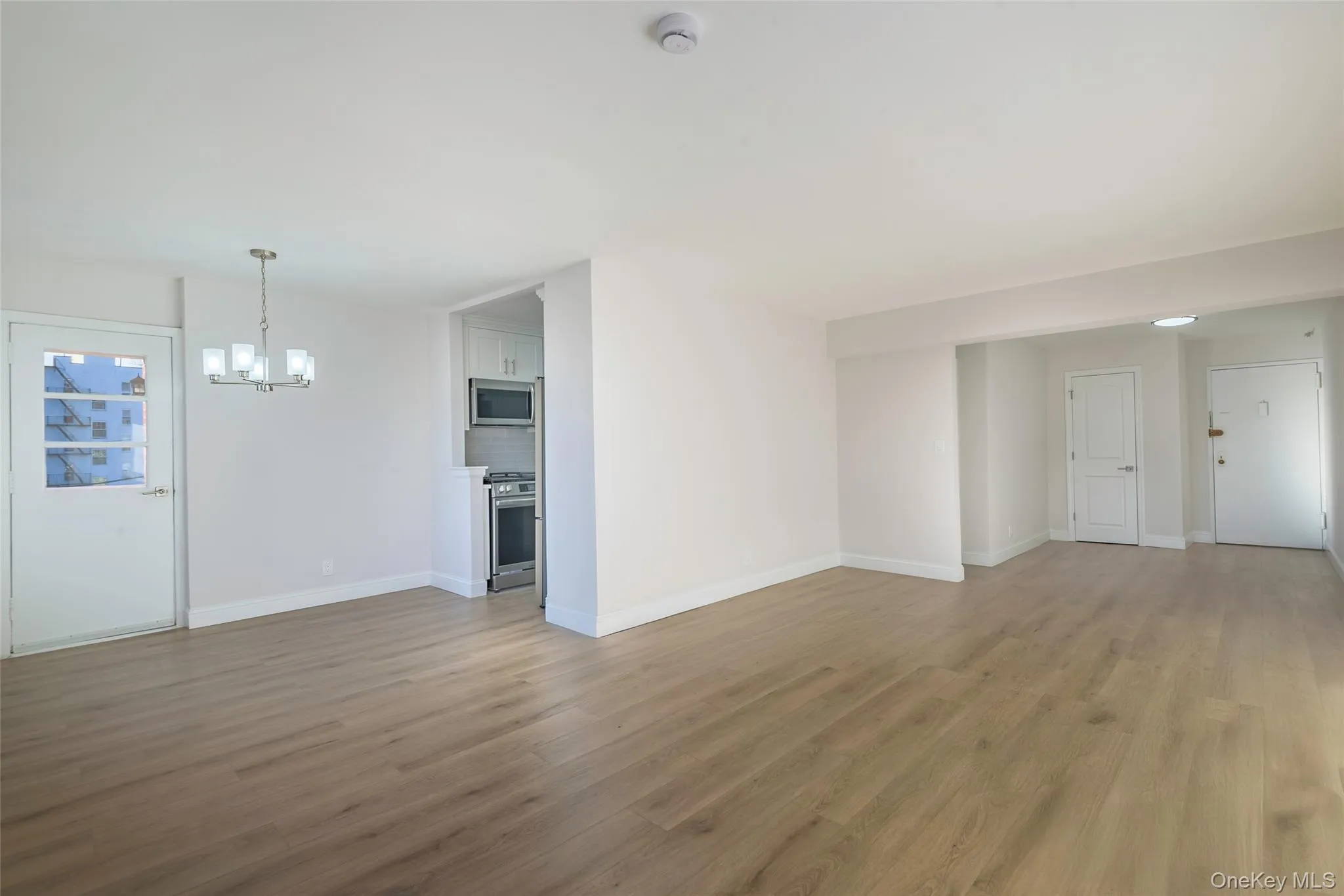 Unfurnished living room featuring light wood finished floors and a chandelier Unfurnished living room featuring light wood finished floors and a chandelier
