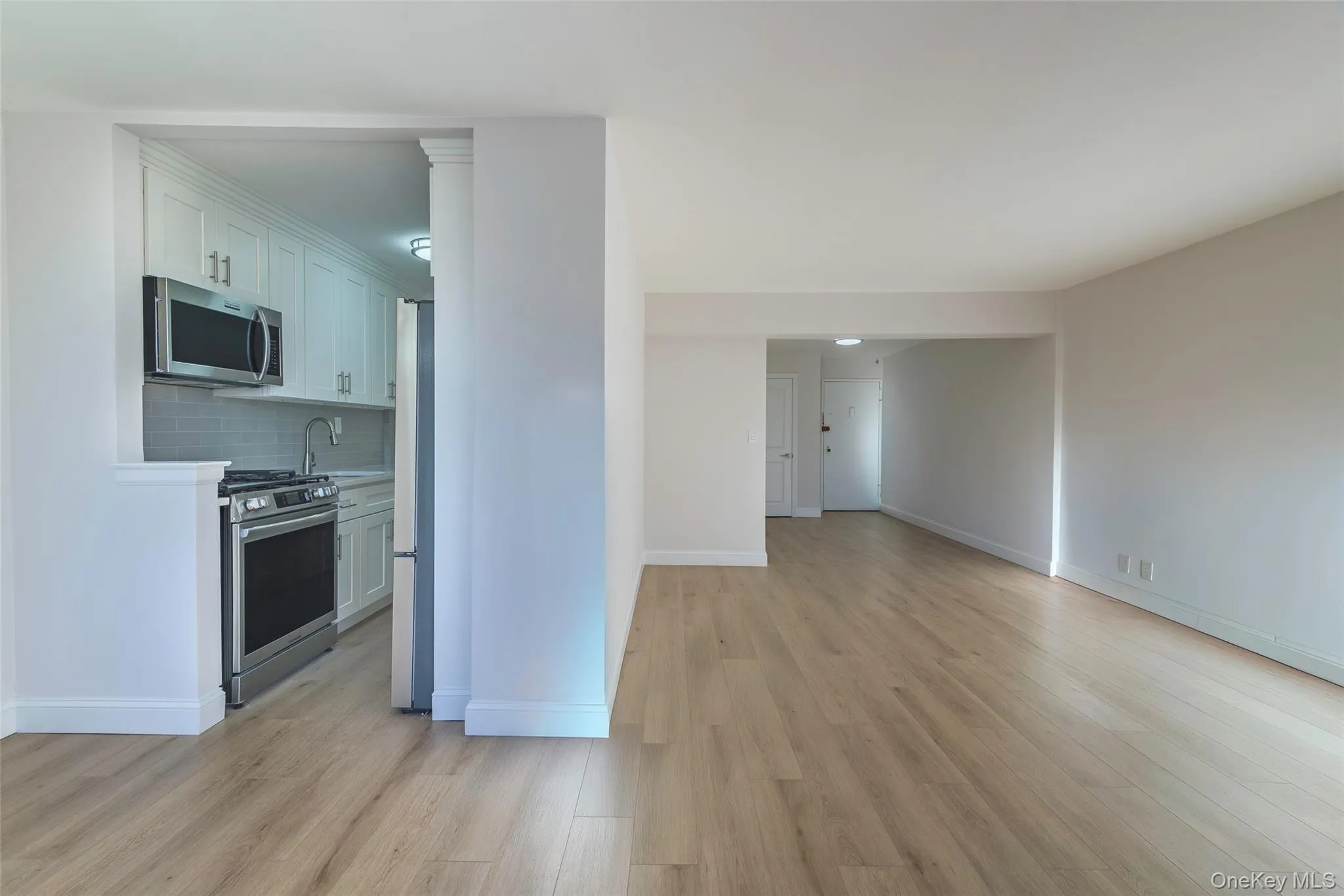Kitchen with stainless steel appliances, light countertops, backsplash, light wood-style flooring, and white cabinets Kitchen with stainless steel appliances, light countertops, backsplash, light wood-style flooring, and white cabinets