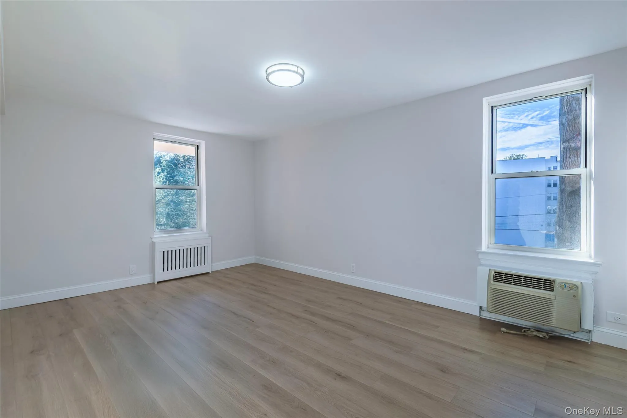 Unfurnished room with light wood-style flooring, radiator heating unit, and an AC wall unit Unfurnished room with light wood-style flooring, radiator heating unit, and an AC wall unit
