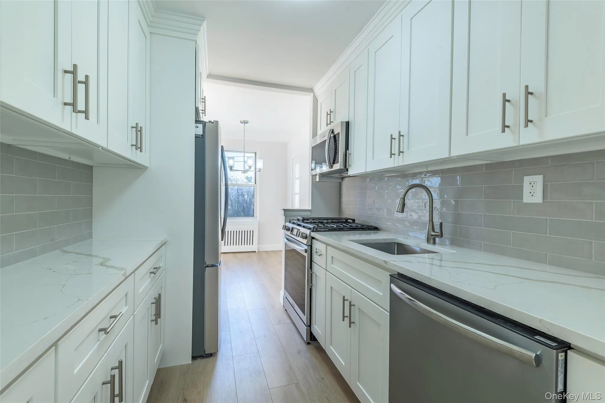 Kitchen featuring light stone counters, stainless steel appliances, decorative light fixtures, and white cabinetry Kitchen featuring light stone counters, stainless steel appliances, decorative light fixtures, and white cabinetry