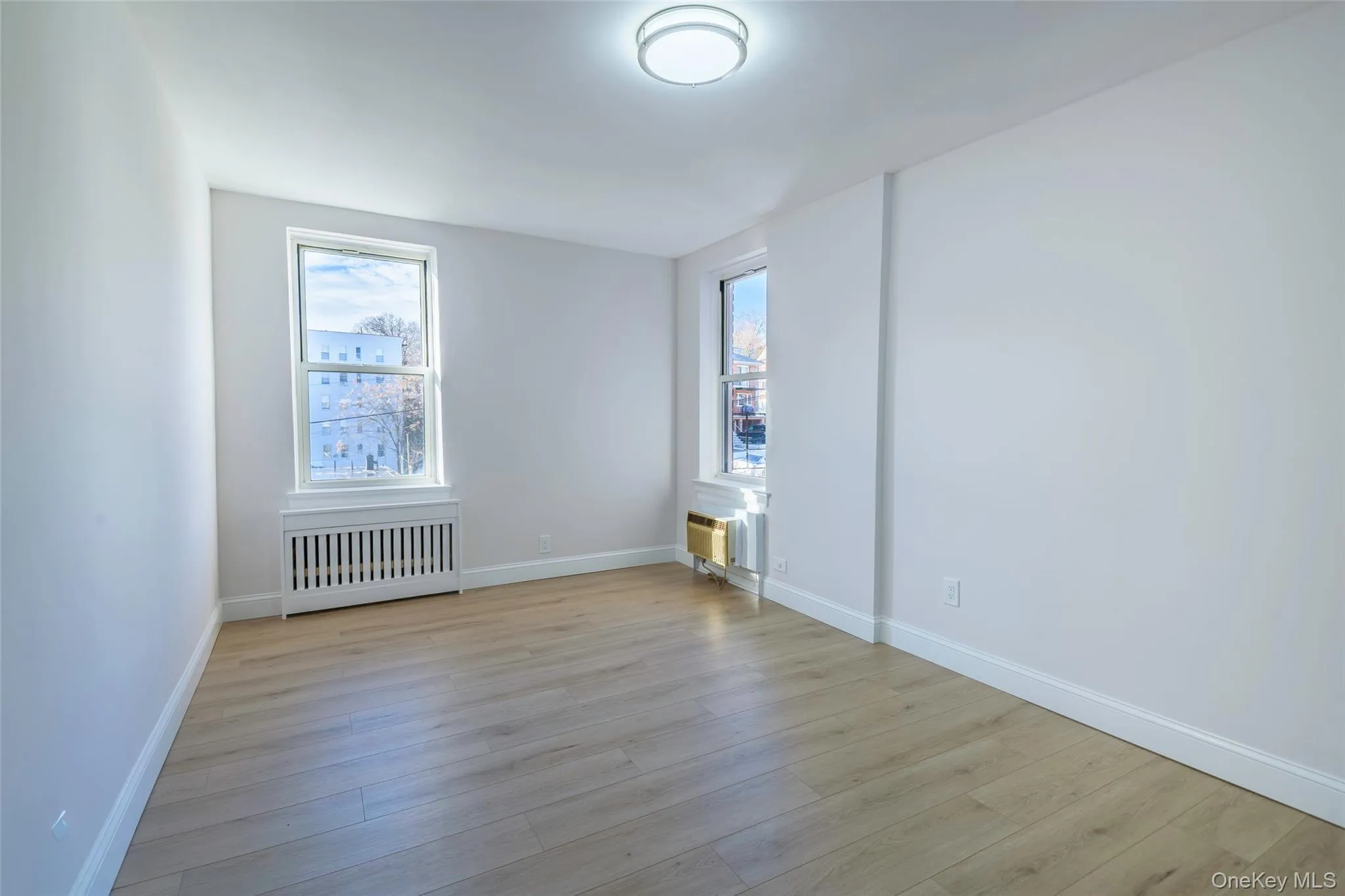 Empty room with plenty of natural light, radiator, and light wood-style flooring Empty room with plenty of natural light, radiator, and light wood-style flooring