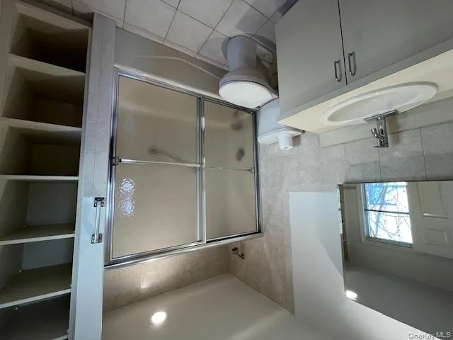Full bath with tile walls, vanity, bath / shower combo with glass door, light tile patterned floors, and recessed lighting Full bath with tile walls, vanity, bath / shower combo with glass door, light tile patterned floors, and recessed lighting