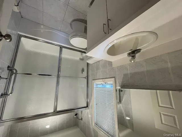 Bathroom featuring tile walls, vanity, bath / shower combo with glass door, and light tile patterned floors Bathroom featuring tile walls, vanity, bath / shower combo with glass door, and light tile patterned floors