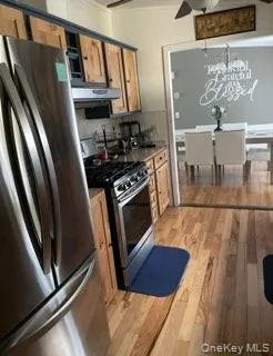 Kitchen with appliances with stainless steel finishes, light wood-type flooring, crown molding, brown cabinets, and a chandelier Kitchen with appliances with stainless steel finishes, light wood-type flooring, crown molding, brown cabinets, and a chandelier