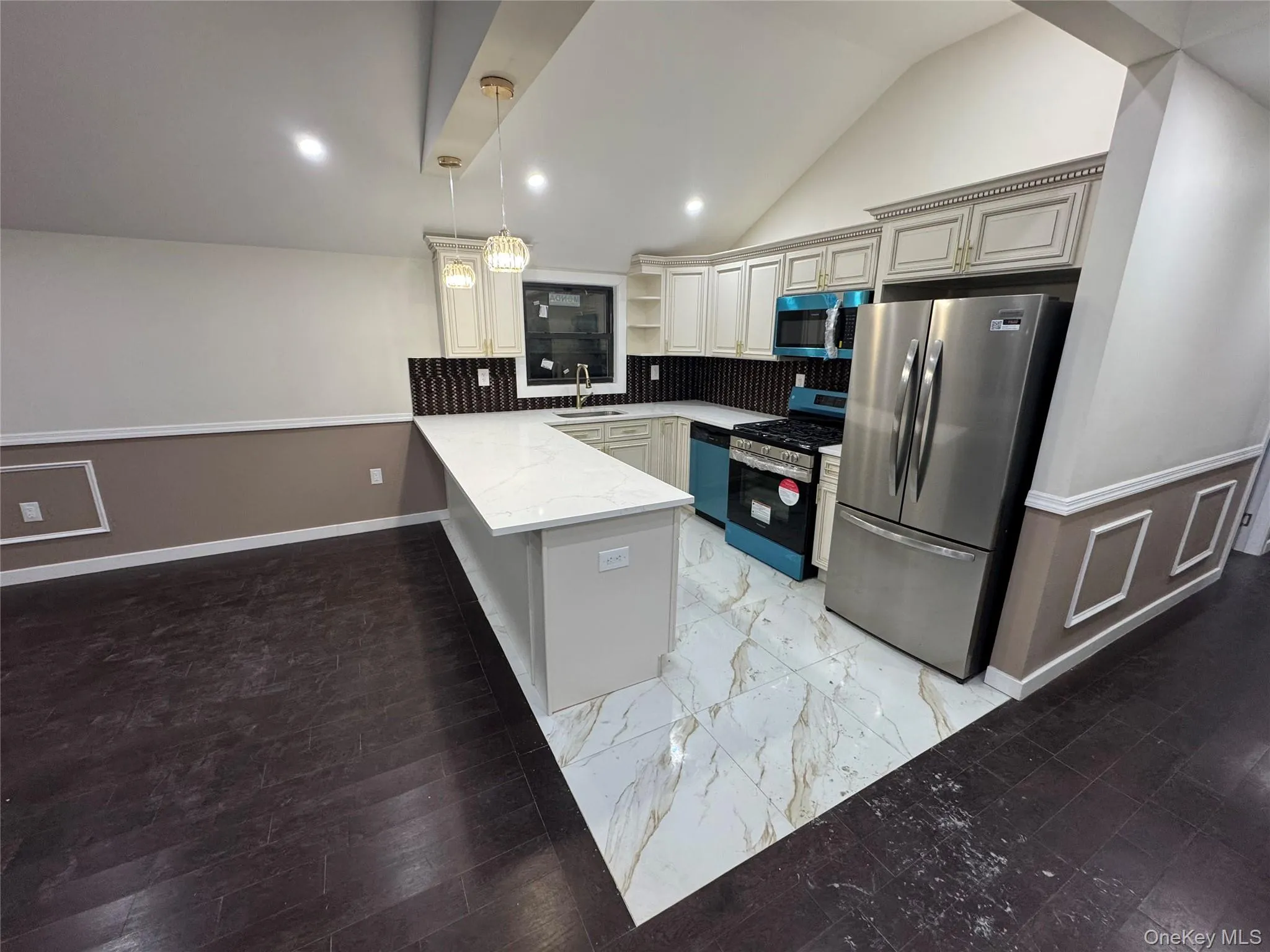 Kitchen with stainless steel appliances, hanging light fixtures, a peninsula, vaulted ceiling, and light marble finish flooring Kitchen with stainless steel appliances, hanging light fixtures, a peninsula, vaulted ceiling, and light marble finish flooring