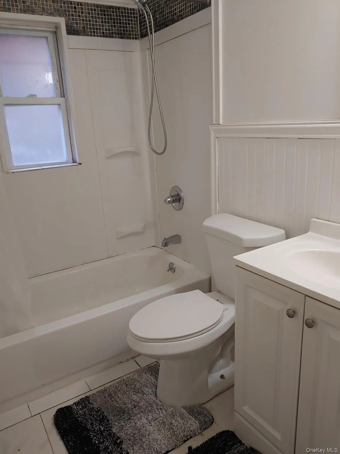 Bathroom with shower / tub combo, light tile patterned flooring, vanity, and a wainscoted wall Bathroom with shower / tub combo, light tile patterned flooring, vanity, and a wainscoted wall