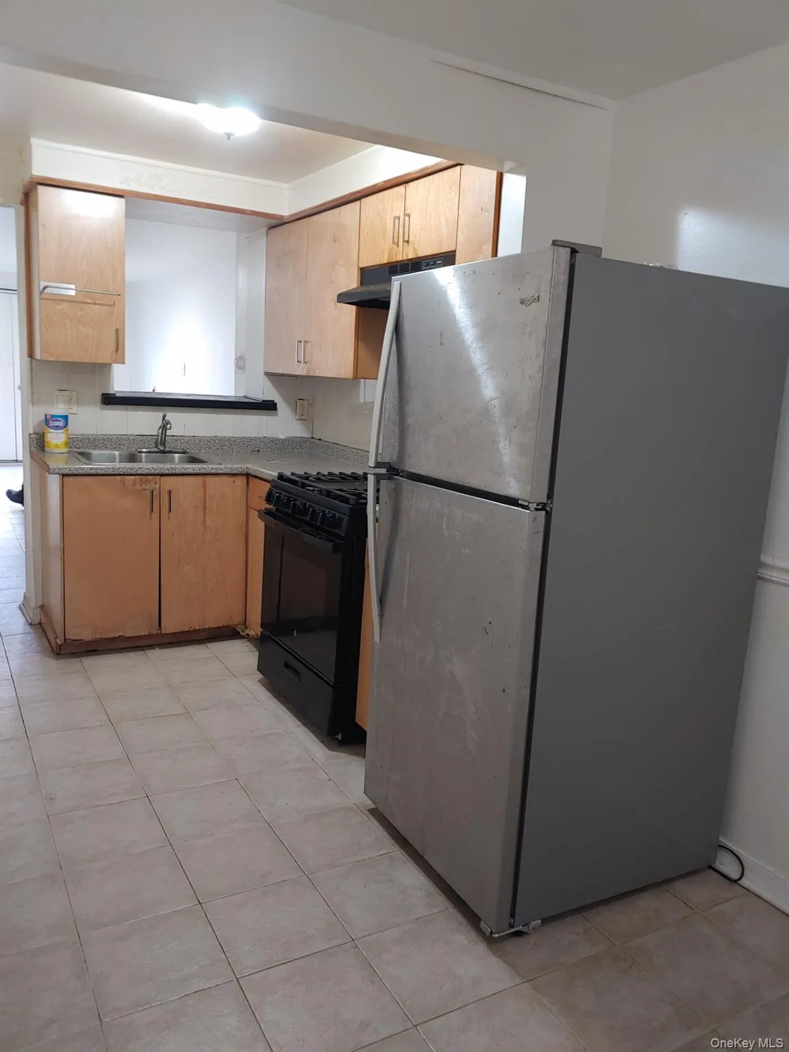 Kitchen featuring freestanding refrigerator, gas stove, light tile patterned flooring, dark countertops, and under cabinet range hood Kitchen featuring freestanding refrigerator, gas stove, light tile patterned flooring, dark countertops, and under cabinet range hood