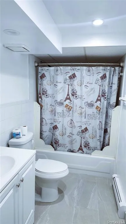 Bathroom with shower / bath combo, vanity, baseboard heating, and tile walls Bathroom with shower / bath combo, vanity, baseboard heating, and tile walls