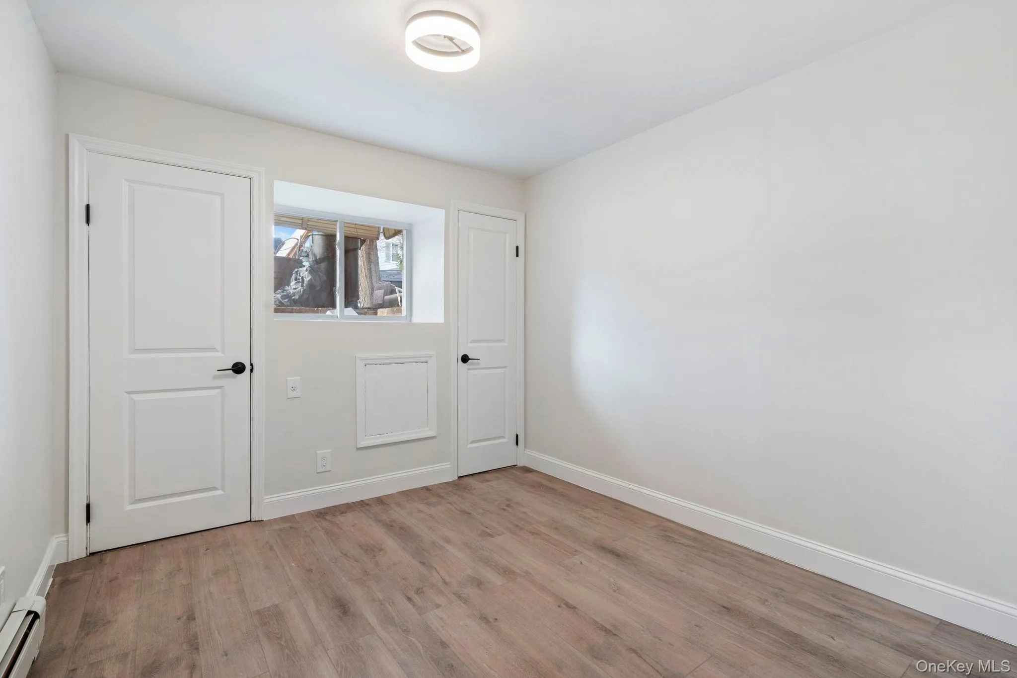 Unfurnished bedroom with light wood finished floors and a baseboard heating unit Unfurnished bedroom with light wood finished floors and a baseboard heating unit