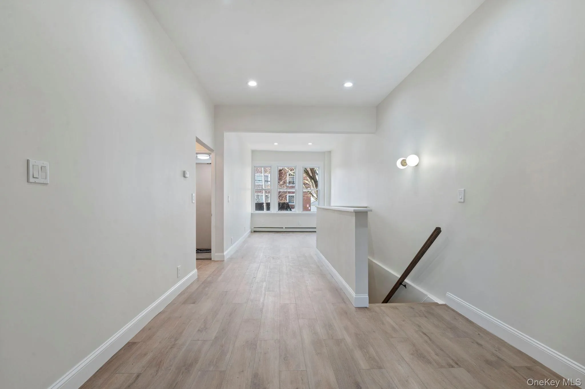 Hallway featuring an upstairs landing, light wood-type flooring, recessed lighting, and a baseboard heating unit Hallway featuring an upstairs landing, light wood-type flooring, recessed lighting, and a baseboard heating unit