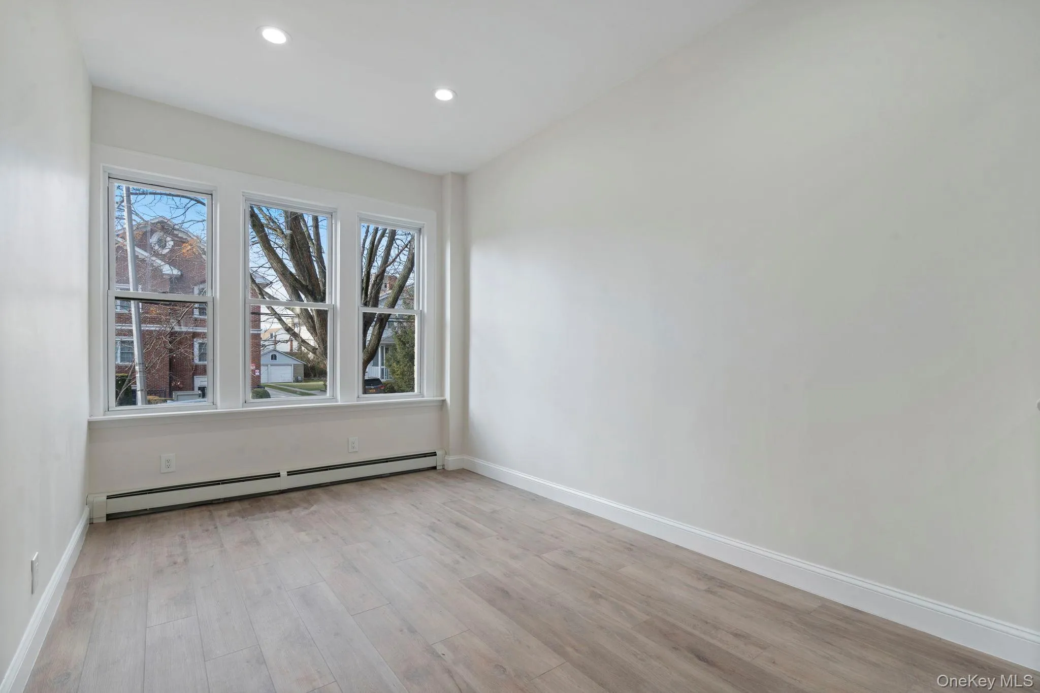 Empty room featuring baseboard heating, light wood-style floors, and recessed lighting Empty room featuring baseboard heating, light wood-style floors, and recessed lighting