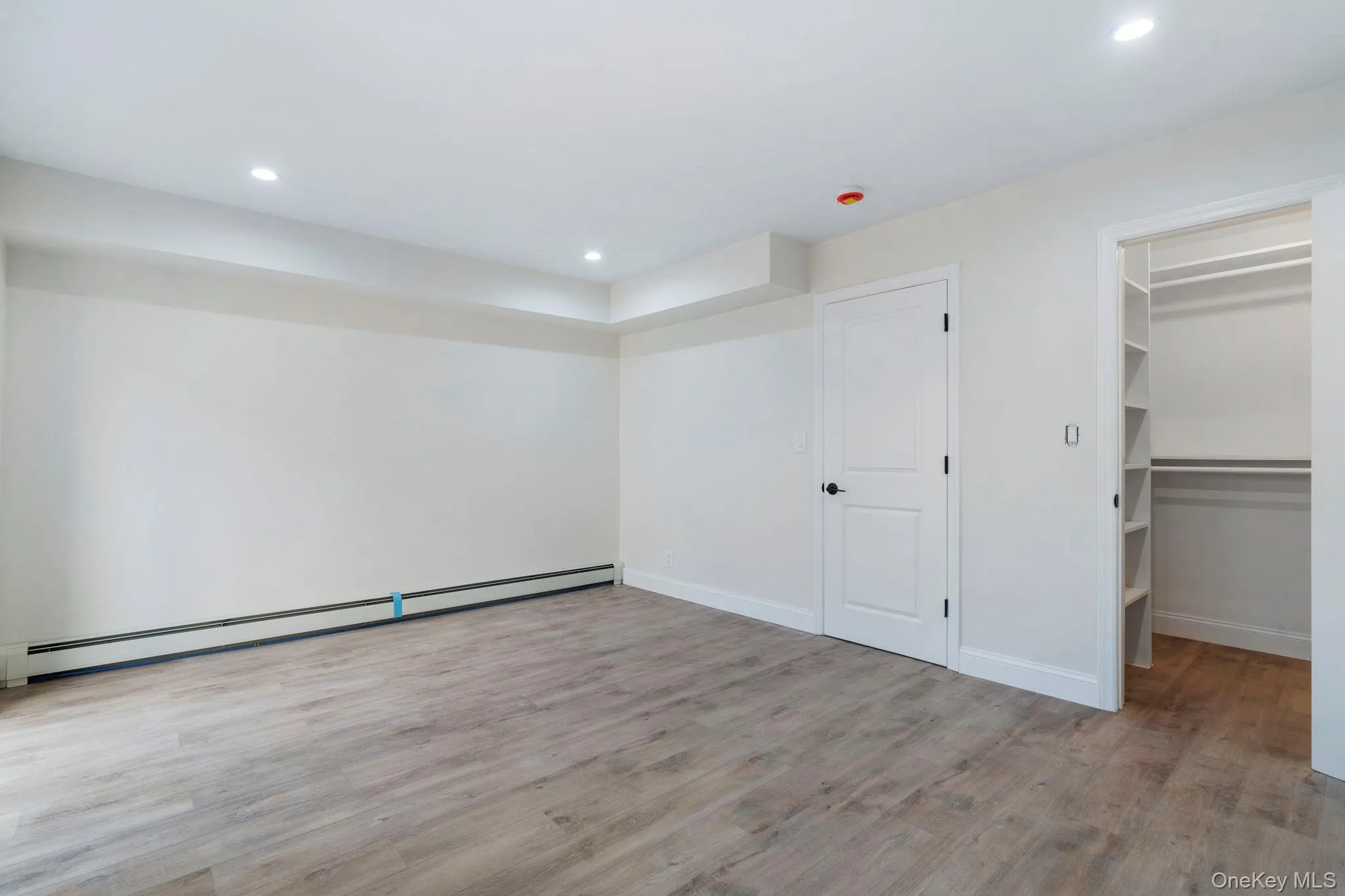 Unfurnished bedroom featuring a walk in closet, a baseboard radiator, light wood-style flooring, and recessed lighting Unfurnished bedroom featuring a walk in closet, a baseboard radiator, light wood-style flooring, and recessed lighting