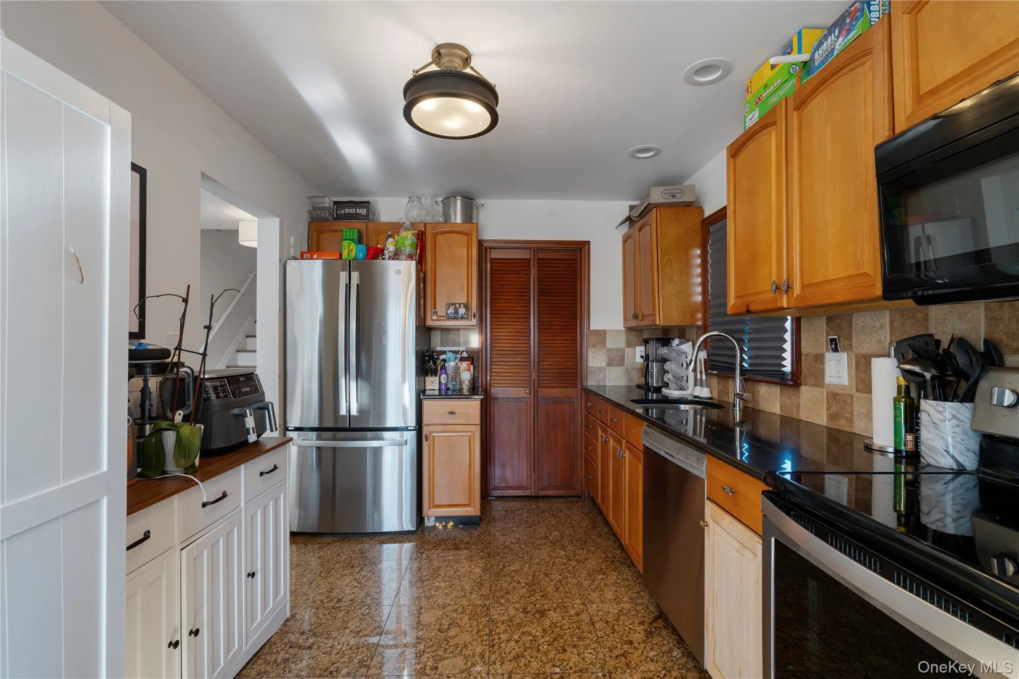 Kitchen with stainless steel appliances, granite tiled floors, decorative backsplash, brown cabinetry, and dark stone countertops Kitchen with stainless steel appliances, granite tiled floors, decorative backsplash, brown cabinetry, and dark stone countertops