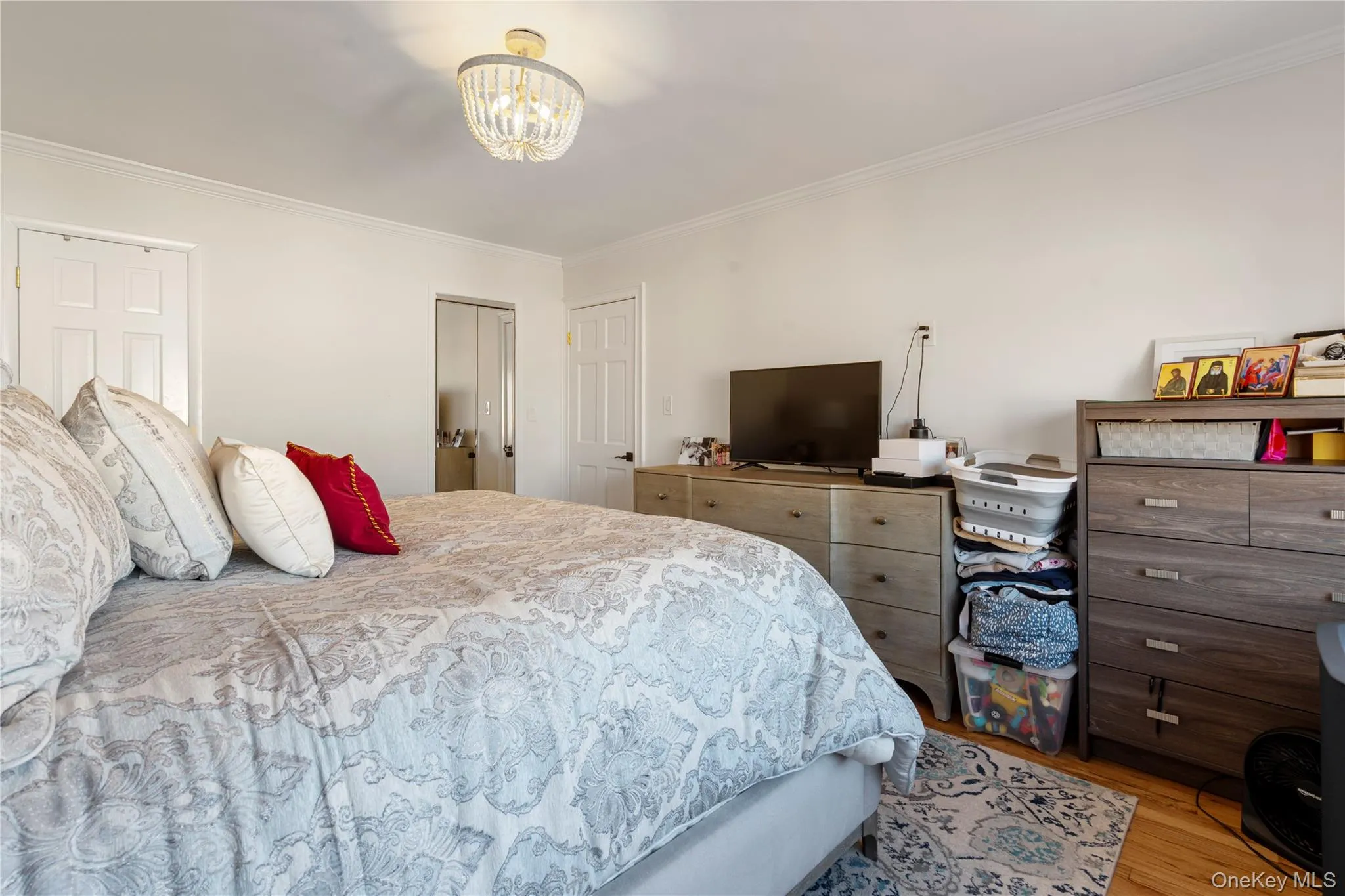 Bedroom featuring crown molding, wood finished floors, a chandelier, and multiple closets Bedroom featuring crown molding, wood finished floors, a chandelier, and multiple closets