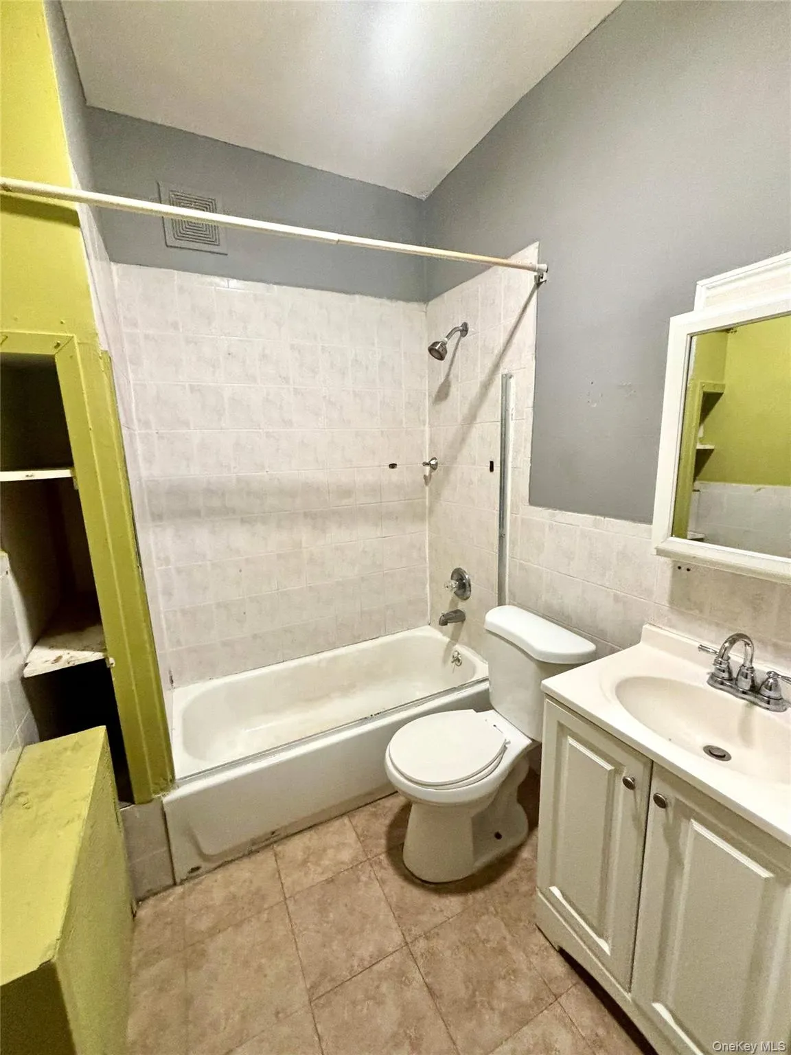 Bathroom featuring vanity, shower / bath combination, tile walls, wainscoting, and light tile patterned flooring Bathroom featuring vanity, shower / bath combination, tile walls, wainscoting, and light tile patterned flooring