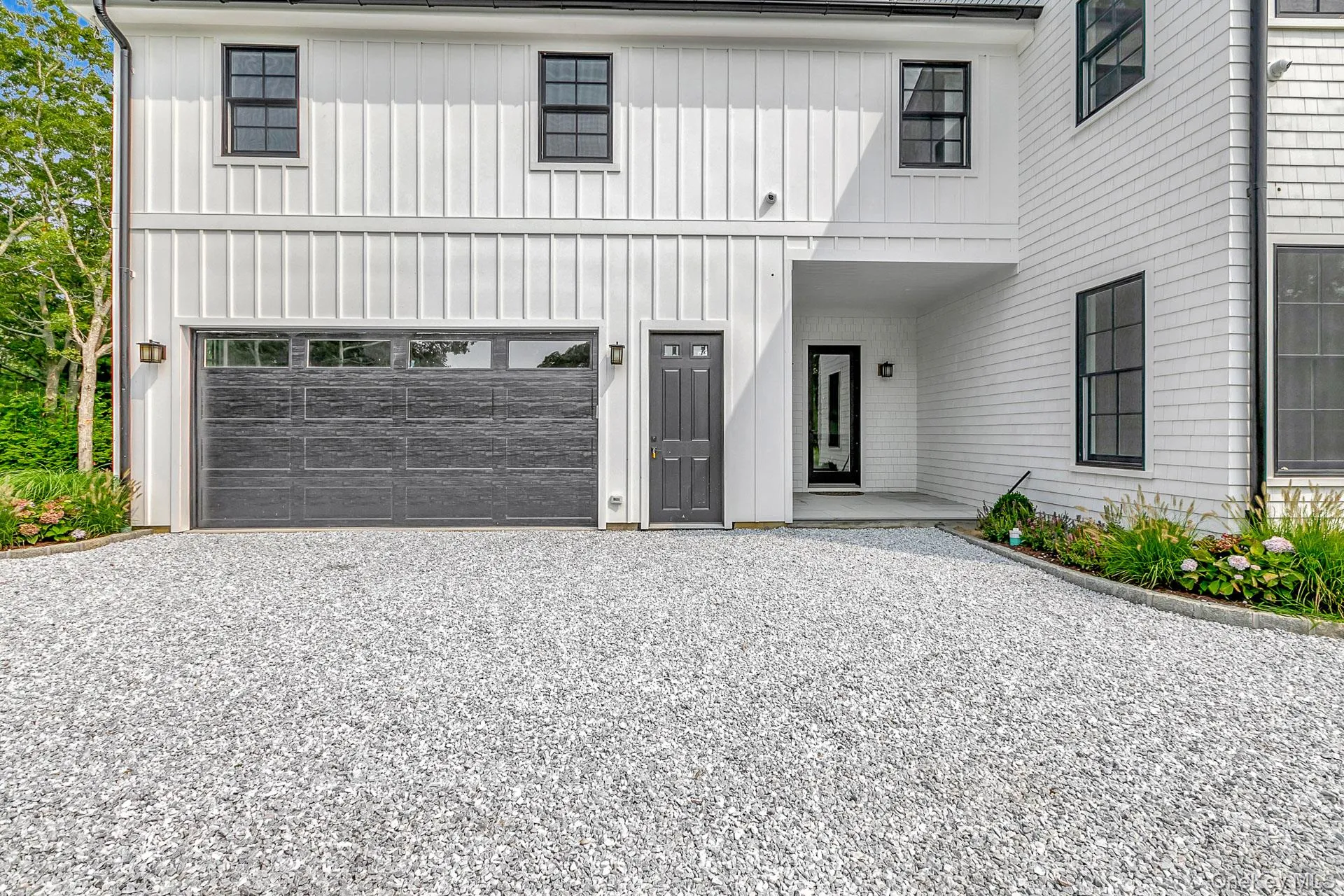 Modern inspired farmhouse with board and batten siding, gravel driveway, covered porch, and an attached garage Modern inspired farmhouse with board and batten siding, gravel driveway, covered porch, and an attached garage