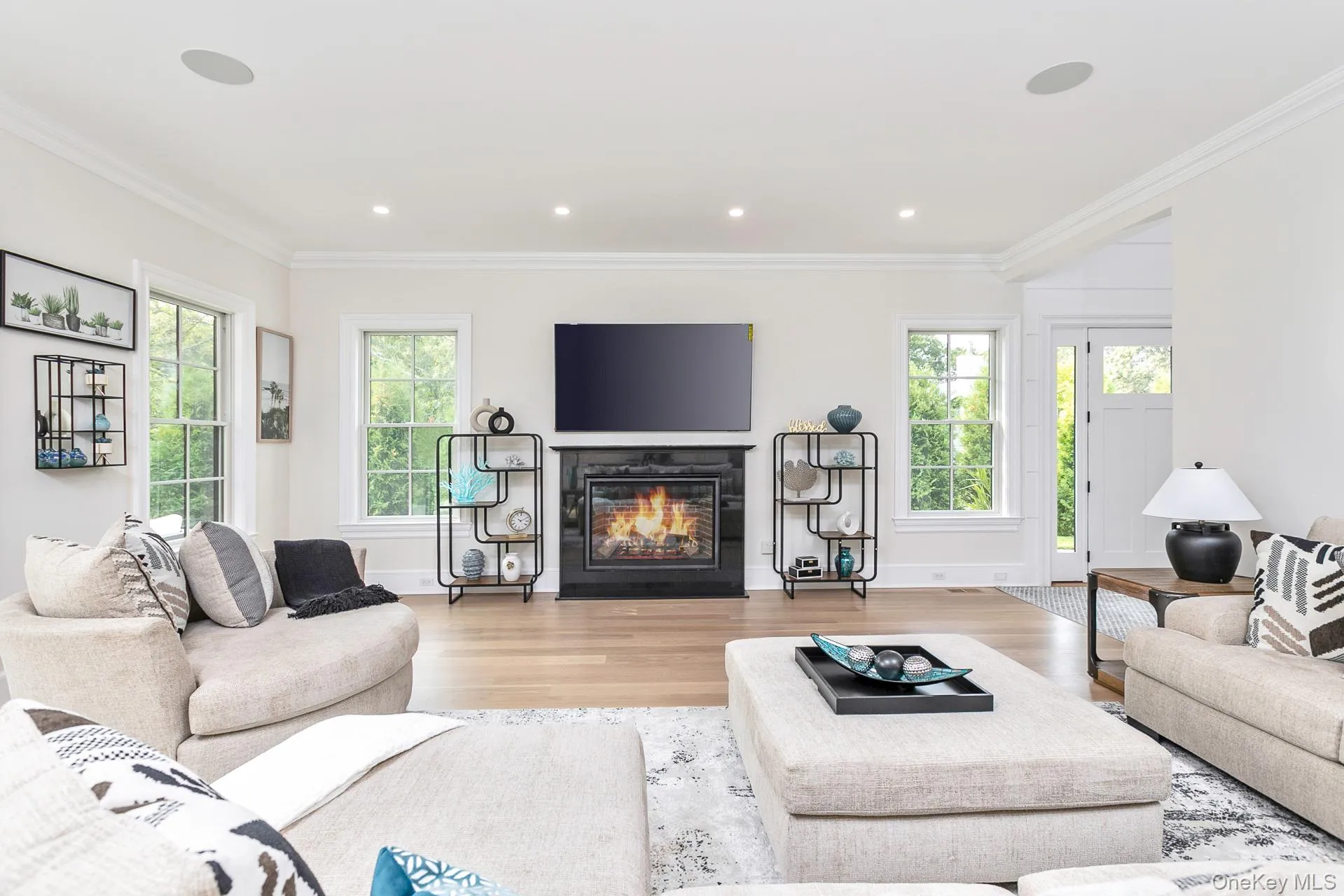 Living room featuring a glass covered fireplace, light wood finished floors, healthy amount of natural light, crown molding, and recessed lighting Living room featuring a glass covered fireplace, light wood finished floors, healthy amount of natural light, crown molding, and recessed lighting