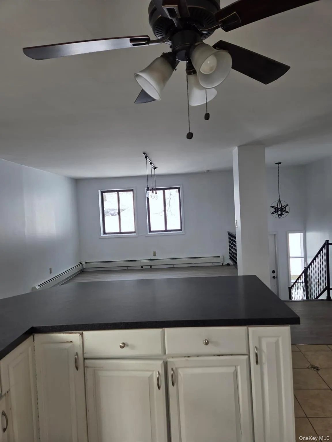 Kitchen featuring open floor plan, dark countertops, pendant lighting, white cabinets, and a baseboard heating unit Kitchen featuring open floor plan, dark countertops, pendant lighting, white cabinets, and a baseboard heating unit