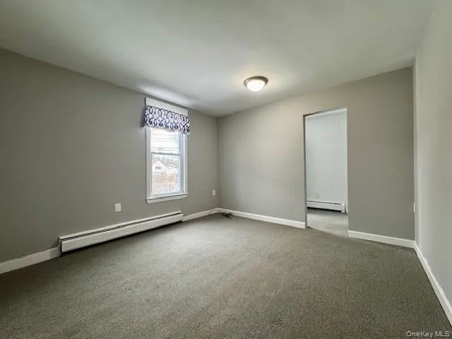 Unfurnished room with a baseboard radiator and carpet floors Unfurnished room with a baseboard radiator and carpet floors
