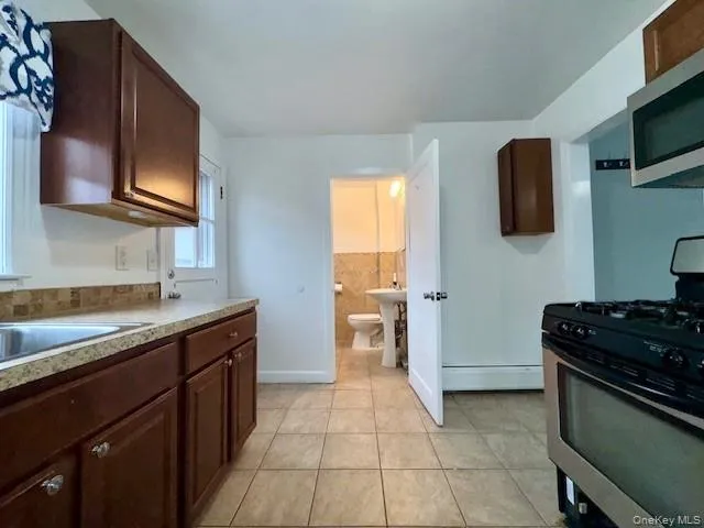 Kitchen featuring appliances with stainless steel finishes, light countertops, a baseboard radiator, light tile patterned floors, and dark brown cabinets Kitchen featuring appliances with stainless steel finishes, light countertops, a baseboard radiator, light tile patterned floors, and dark brown cabinets