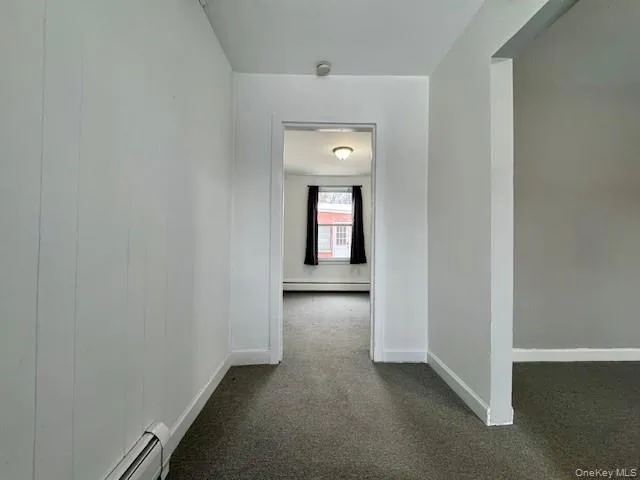 Hallway featuring a baseboard heating unit and dark colored carpet Hallway featuring a baseboard heating unit and dark colored carpet