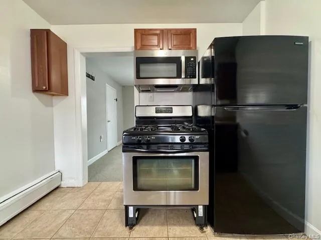 Kitchen with stainless steel appliances, baseboard heating, light tile patterned floors, and brown cabinetry Kitchen with stainless steel appliances, baseboard heating, light tile patterned floors, and brown cabinetry