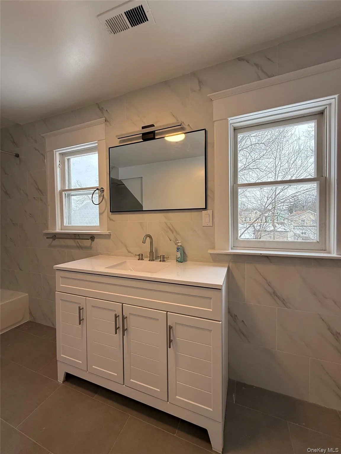 Bathroom with tile walls, vanity, dark tile patterned flooring, and bathtub / shower combination Bathroom with tile walls, vanity, dark tile patterned flooring, and bathtub / shower combination