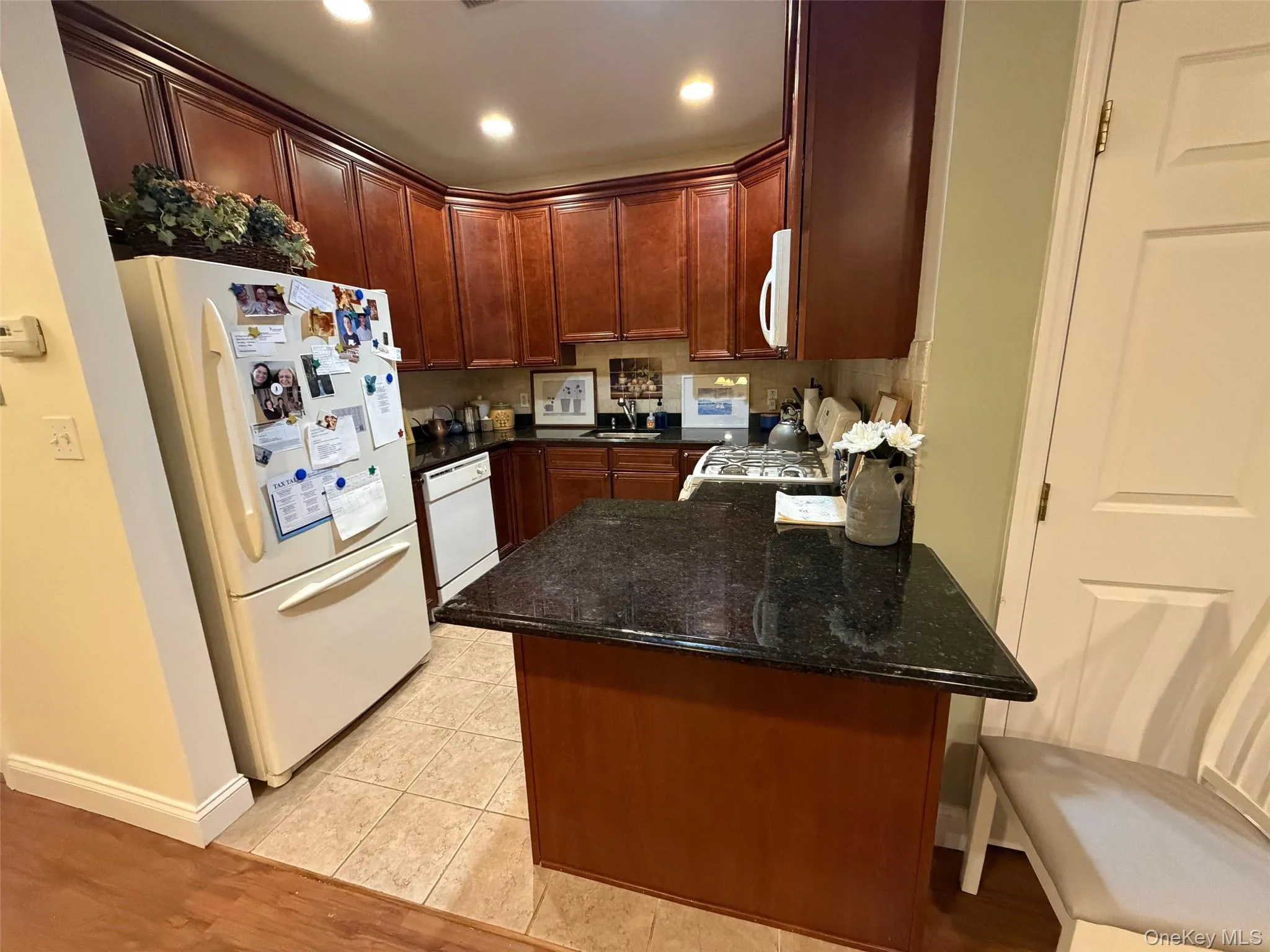 Kitchen with white appliances, dark stone counters, light wood-style flooring, a peninsula, and recessed lighting Kitchen with white appliances, dark stone counters, light wood-style flooring, a peninsula, and recessed lighting