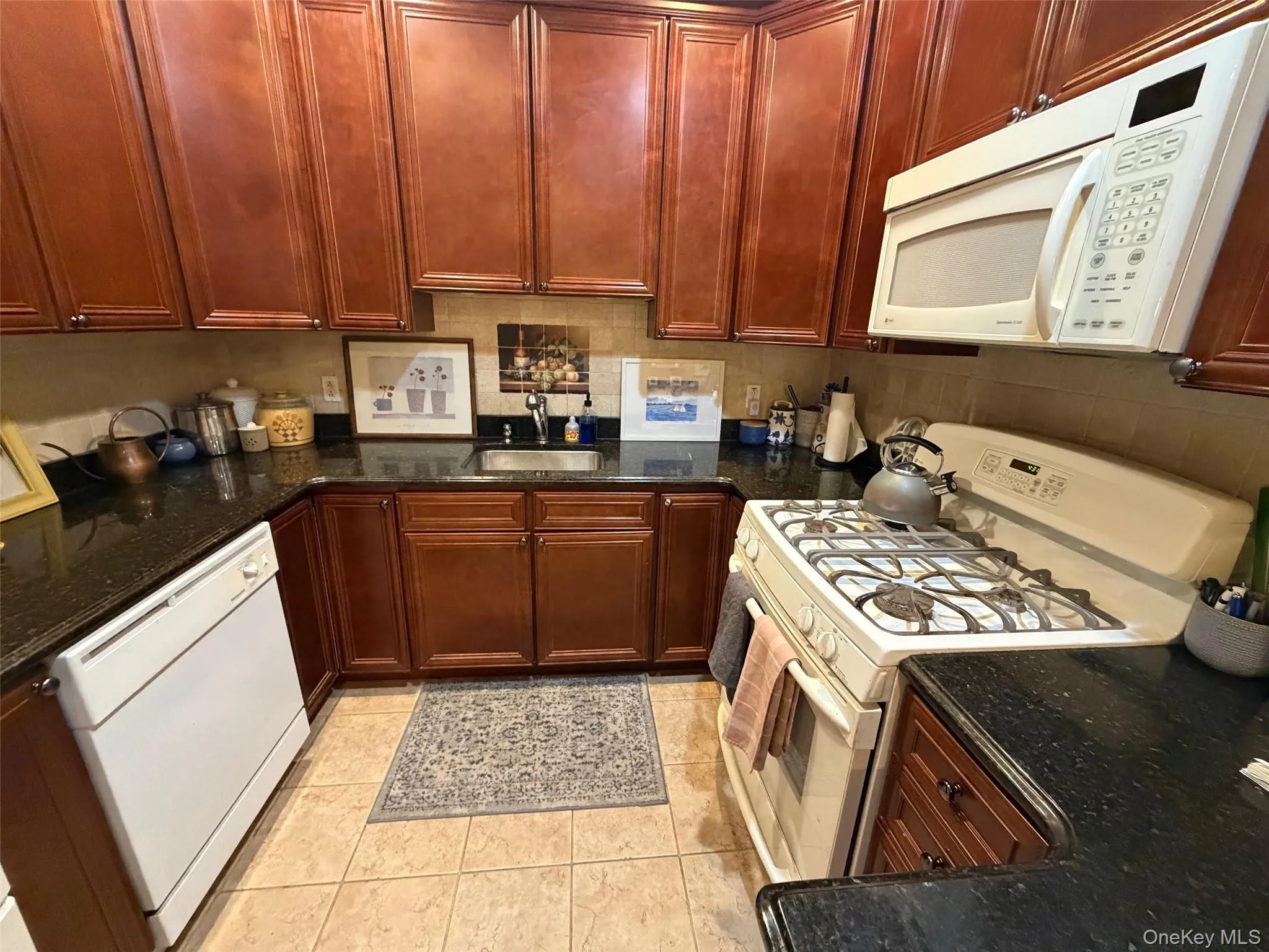 Kitchen with white appliances, dark stone counters, and light tile patterned flooring Kitchen with white appliances, dark stone counters, and light tile patterned flooring