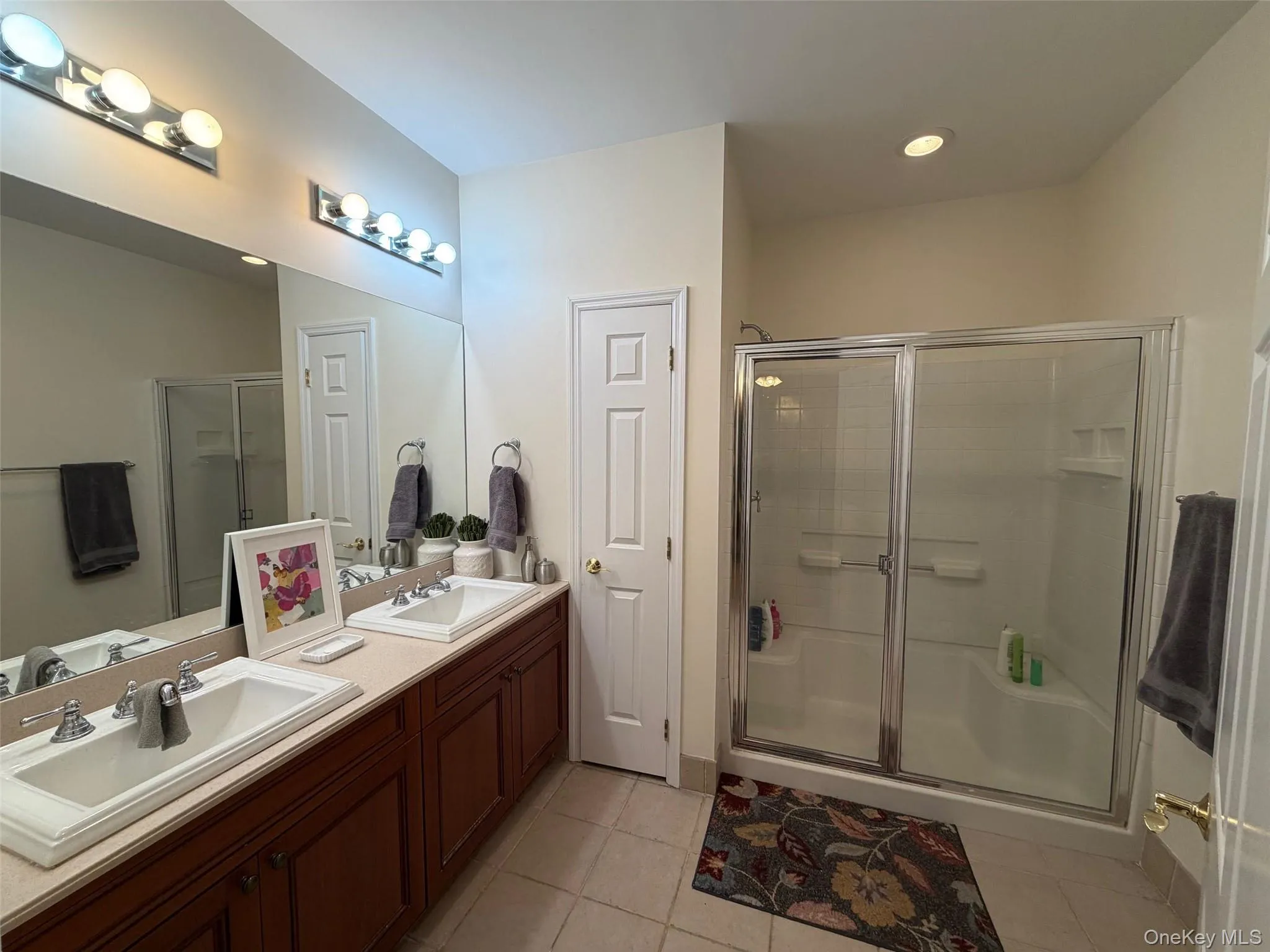 Bathroom featuring a shower stall, double vanity, light tile patterned floors, and recessed lighting Bathroom featuring a shower stall, double vanity, light tile patterned floors, and recessed lighting