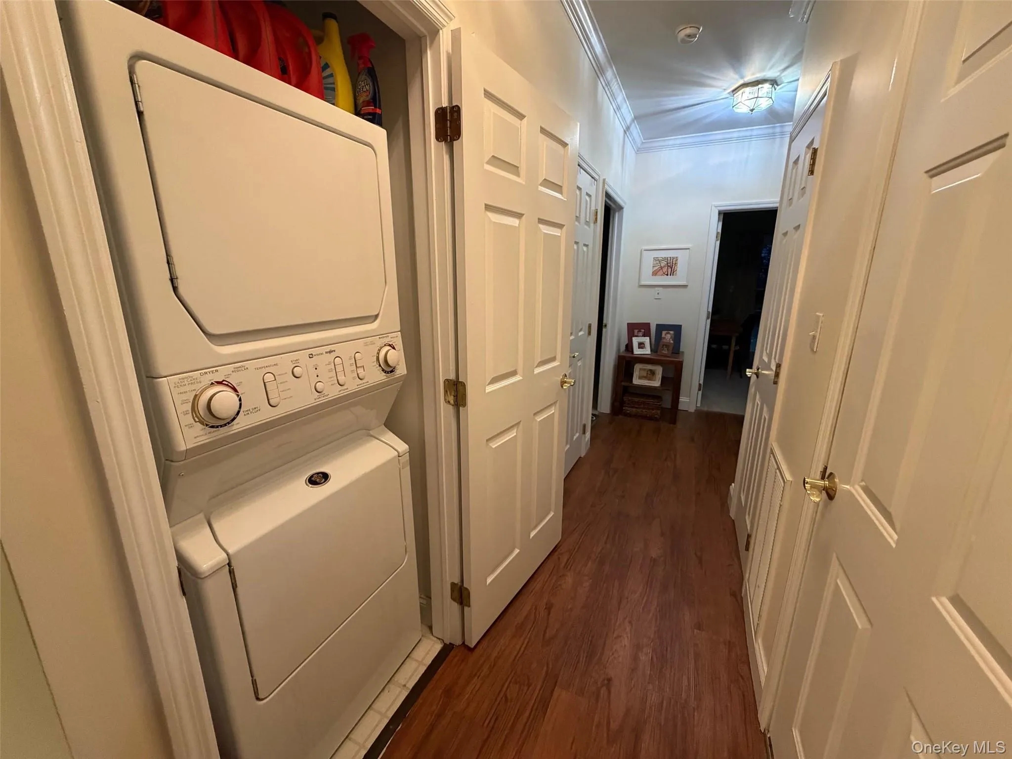 Laundry room featuring dark wood-style flooring, crown molding, and stacked washing machine and dryer Laundry room featuring dark wood-style flooring, crown molding, and stacked washing machine and dryer
