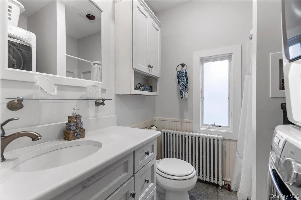 Bathroom with curtained shower, radiator, washer / clothes dryer, wainscoting, and vanity Bathroom with curtained shower, radiator, washer / clothes dryer, wainscoting, and vanity