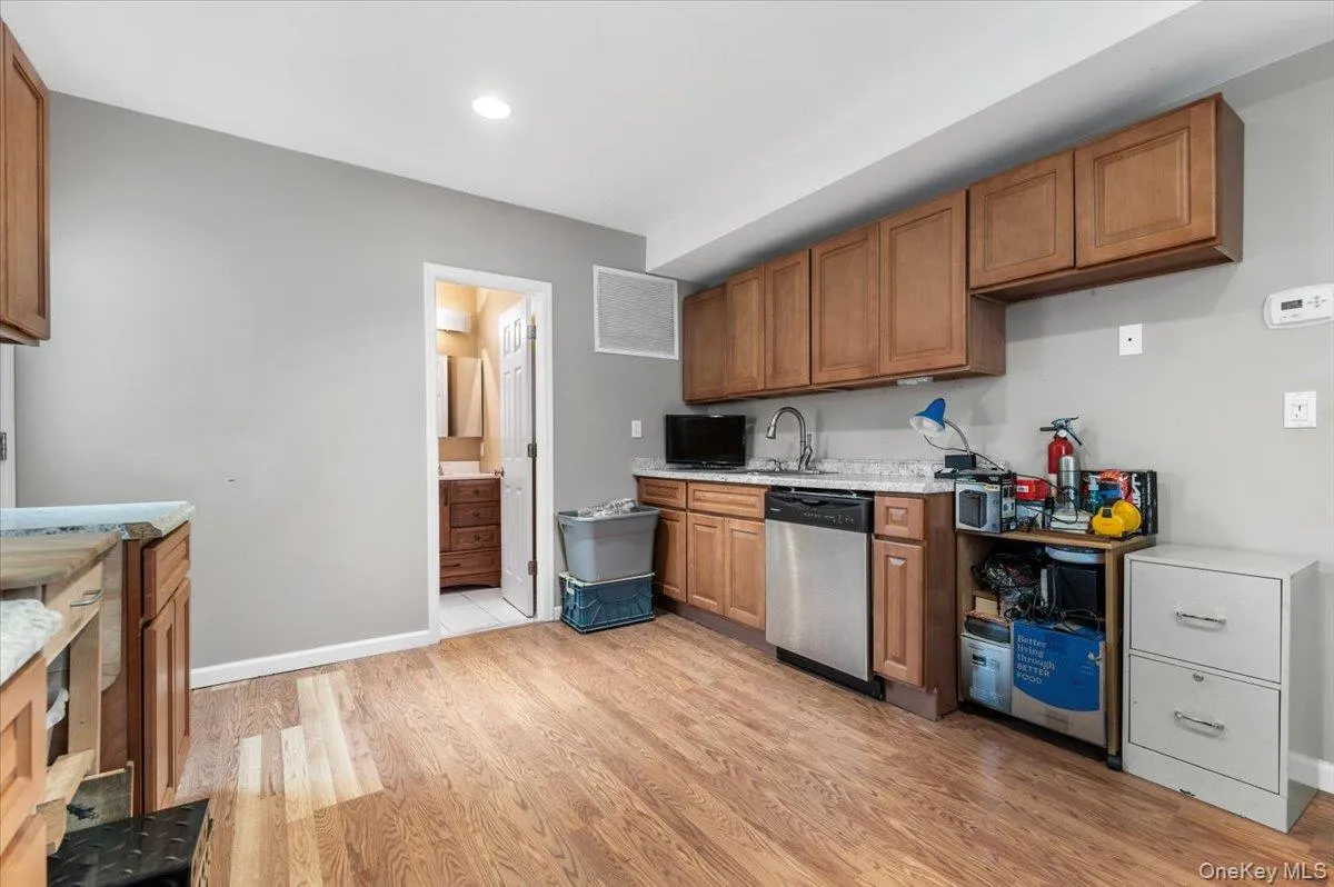 Kitchen with brown cabinets, dishwasher, light wood-style flooring, and light stone counters Kitchen with brown cabinets, dishwasher, light wood-style flooring, and light stone counters