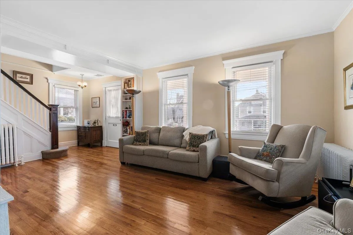 Living area with stairs, radiator, wood-type flooring, crown molding, and a chandelier Living area with stairs, radiator, wood-type flooring, crown molding, and a chandelier