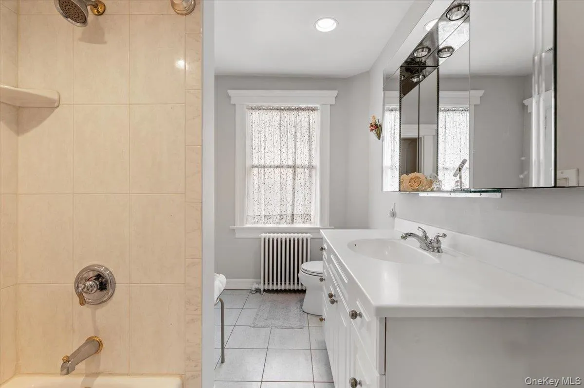 Full bath featuring vanity, radiator heating unit, light tile patterned floors, shower / bath combination, and healthy amount of natural light Full bath featuring vanity, radiator heating unit, light tile patterned floors, shower / bath combination, and healthy amount of natural light